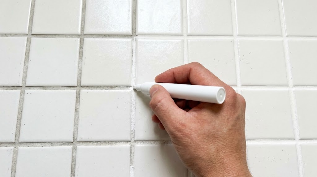 Mike Holmes home fixes: hand using a white grout pen on dingy tile grout lines