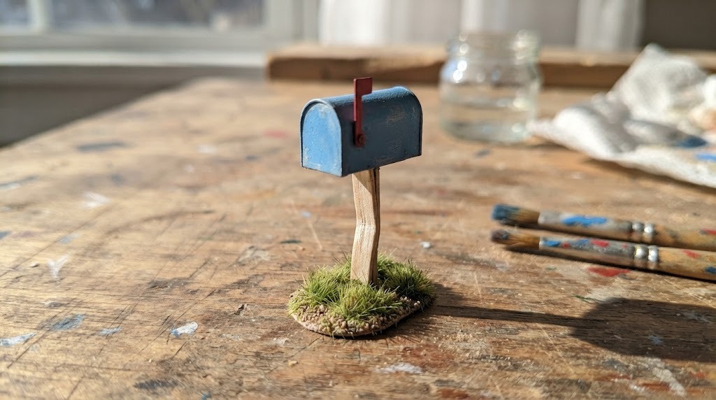 Tiny blue vintage mailbox miniature with a red flag on a patch of grass