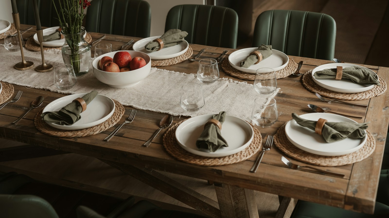 Farmhouse table set with white plates, rolled green linen napkins and a bowl of red apples