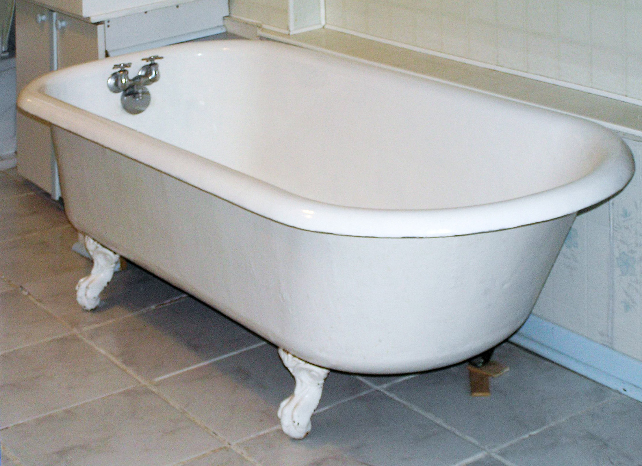 Old house features clawfoot bathtub with curved rim and claw feet on a tile floor