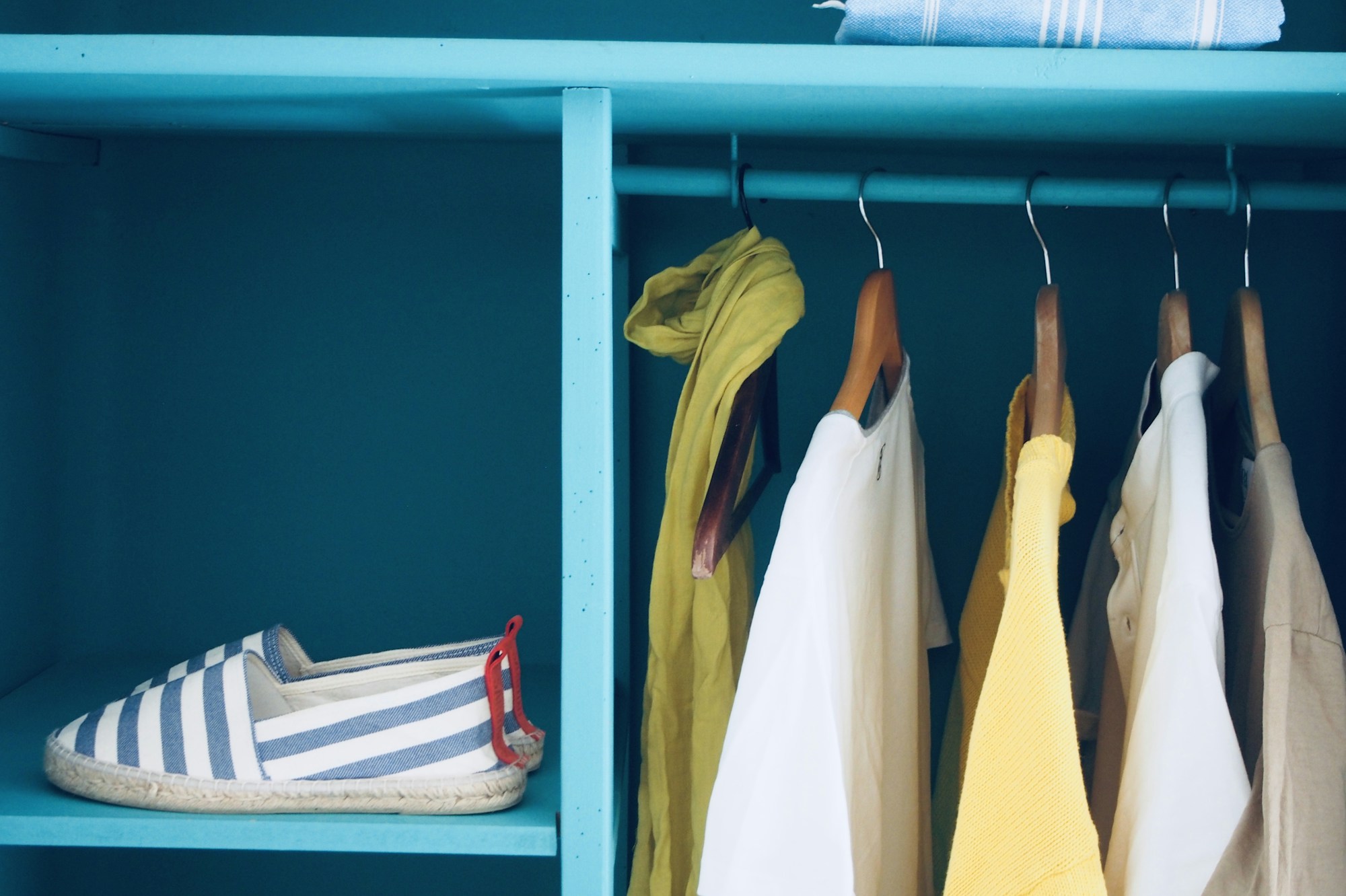 Bright blue painted closet with hanging clothes and a shoe shelf