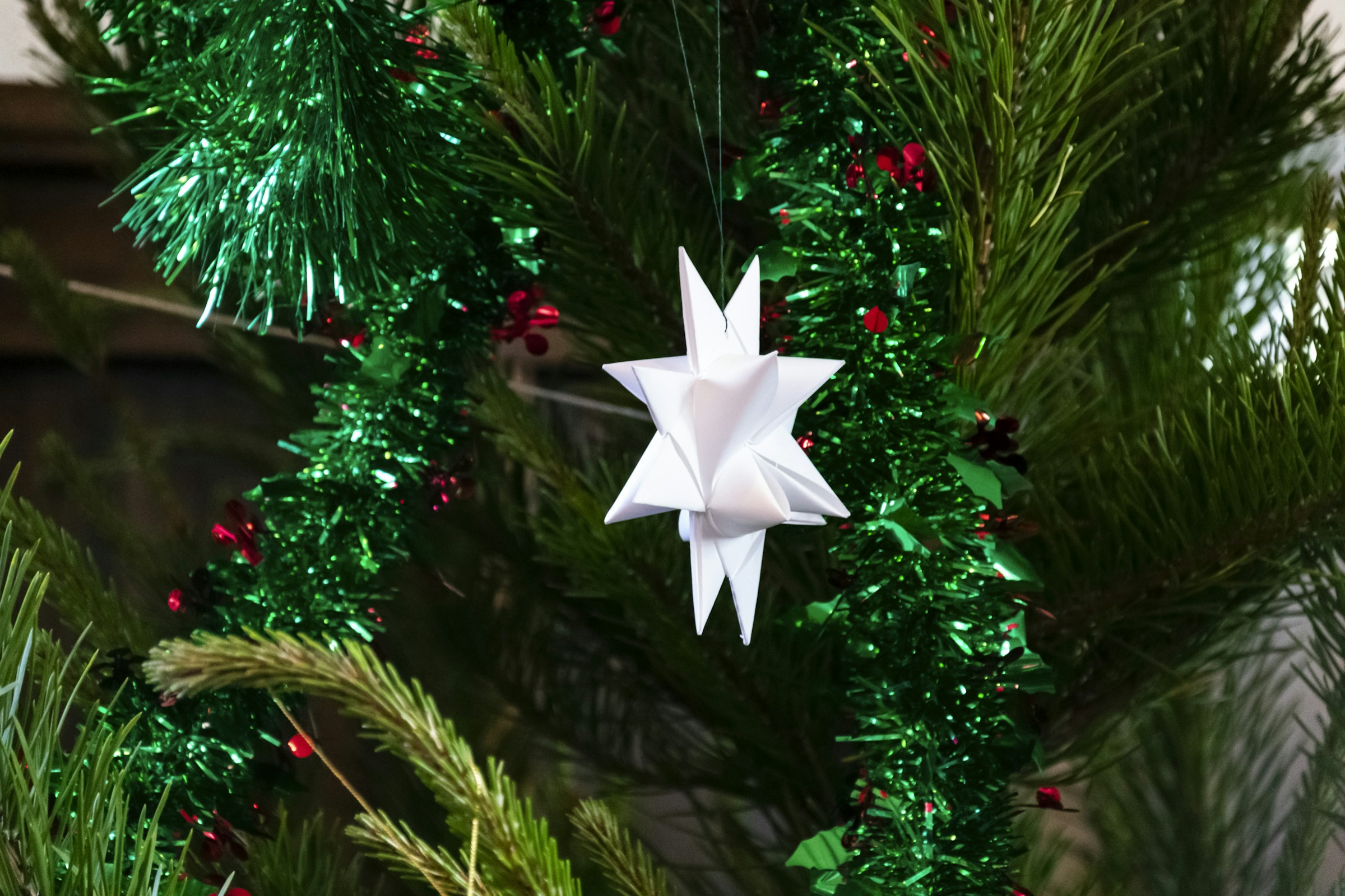 White folded paper origami star ornament hanging on a Christmas tree