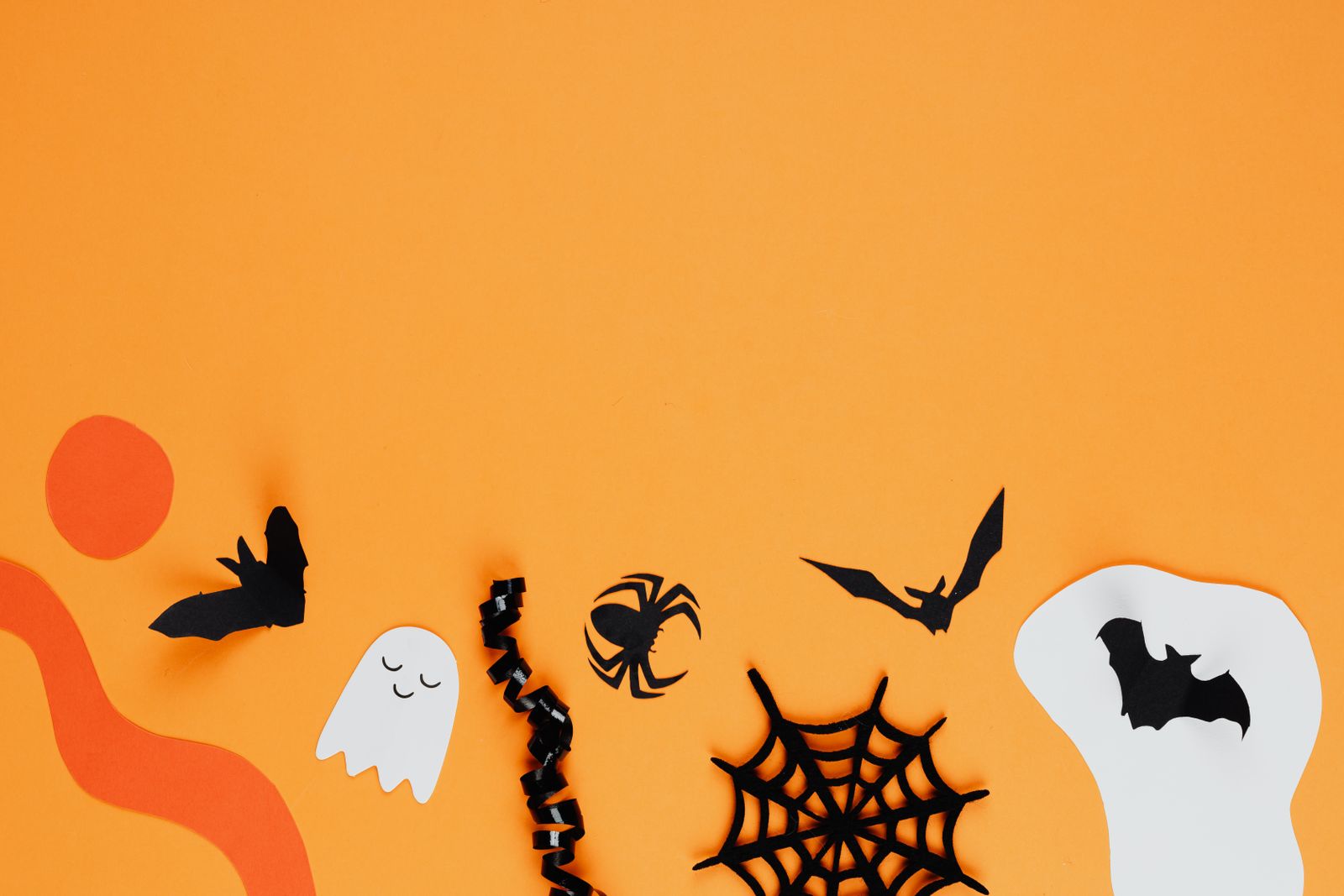 Paper bat, ghost, spider and web cutouts on an orange background