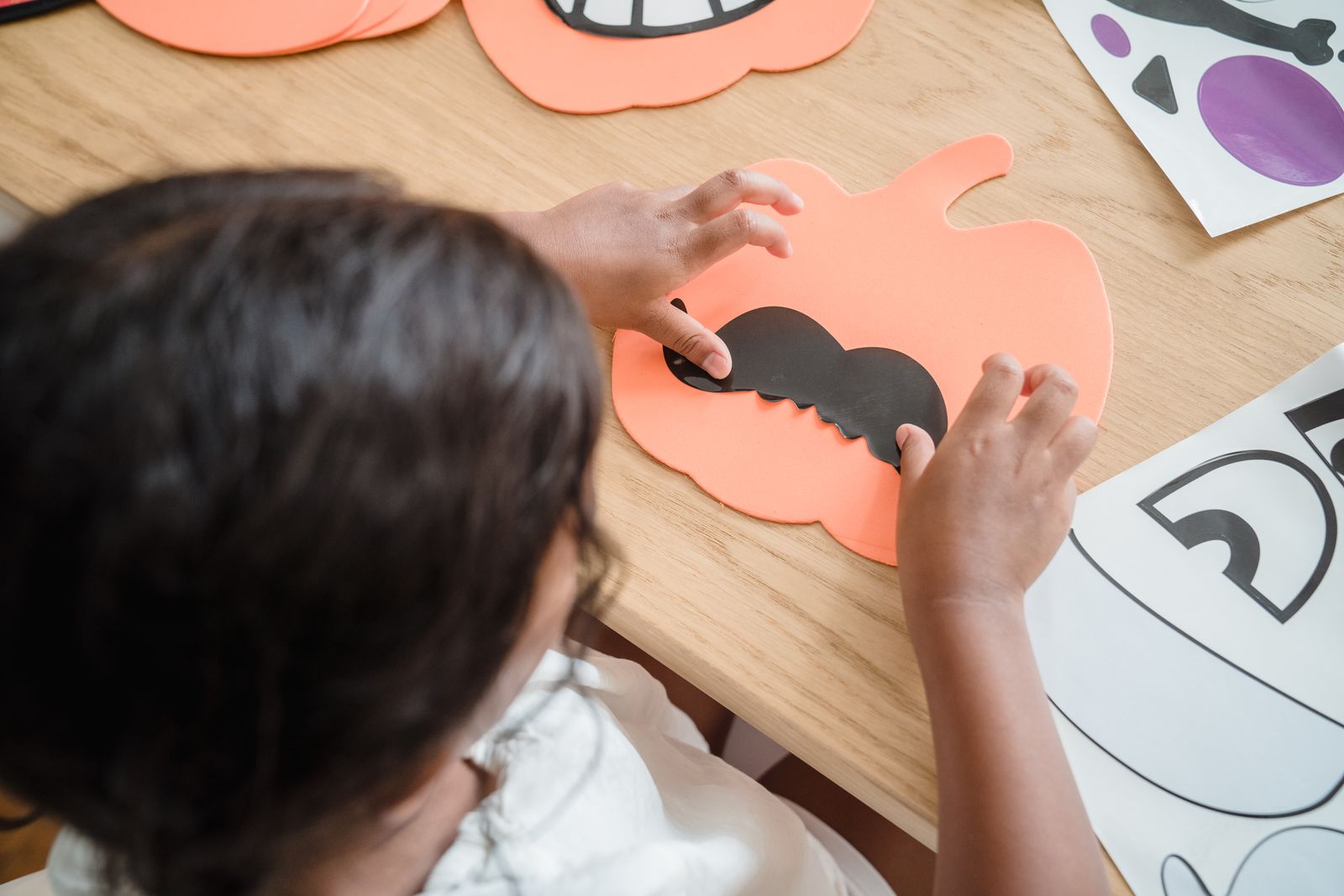 Child gluing paper features onto an orange paper pumpkin face