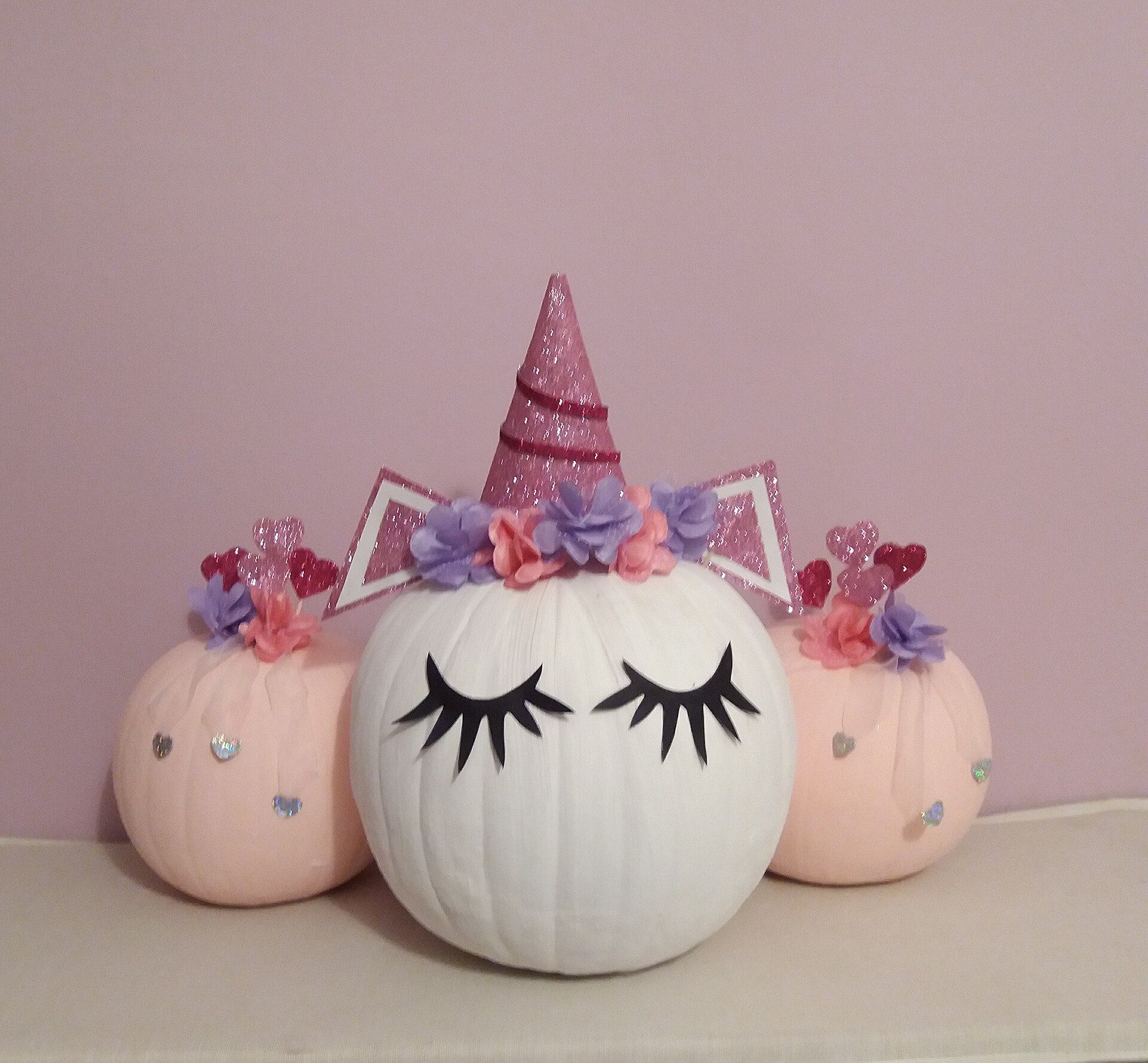 White and pink unicorn pumpkins with glitter horns, flowers and painted lashes