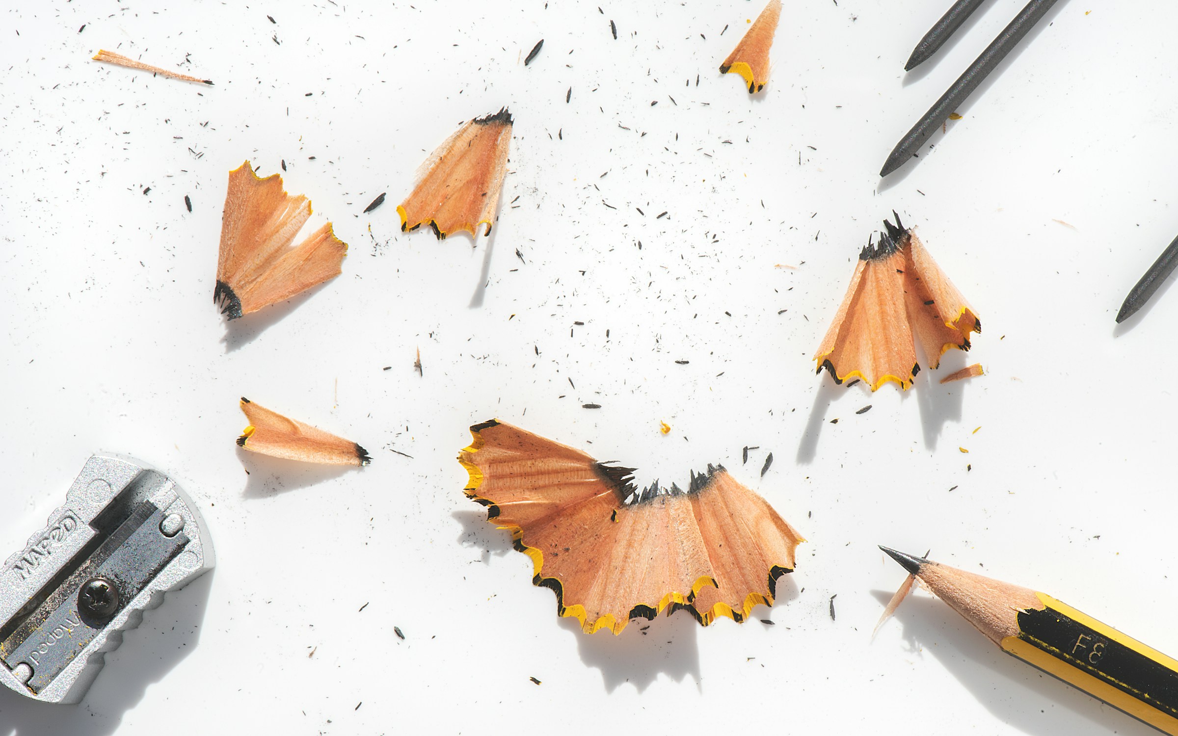Pencil shavings scattered beside a sharpener and yellow pencil