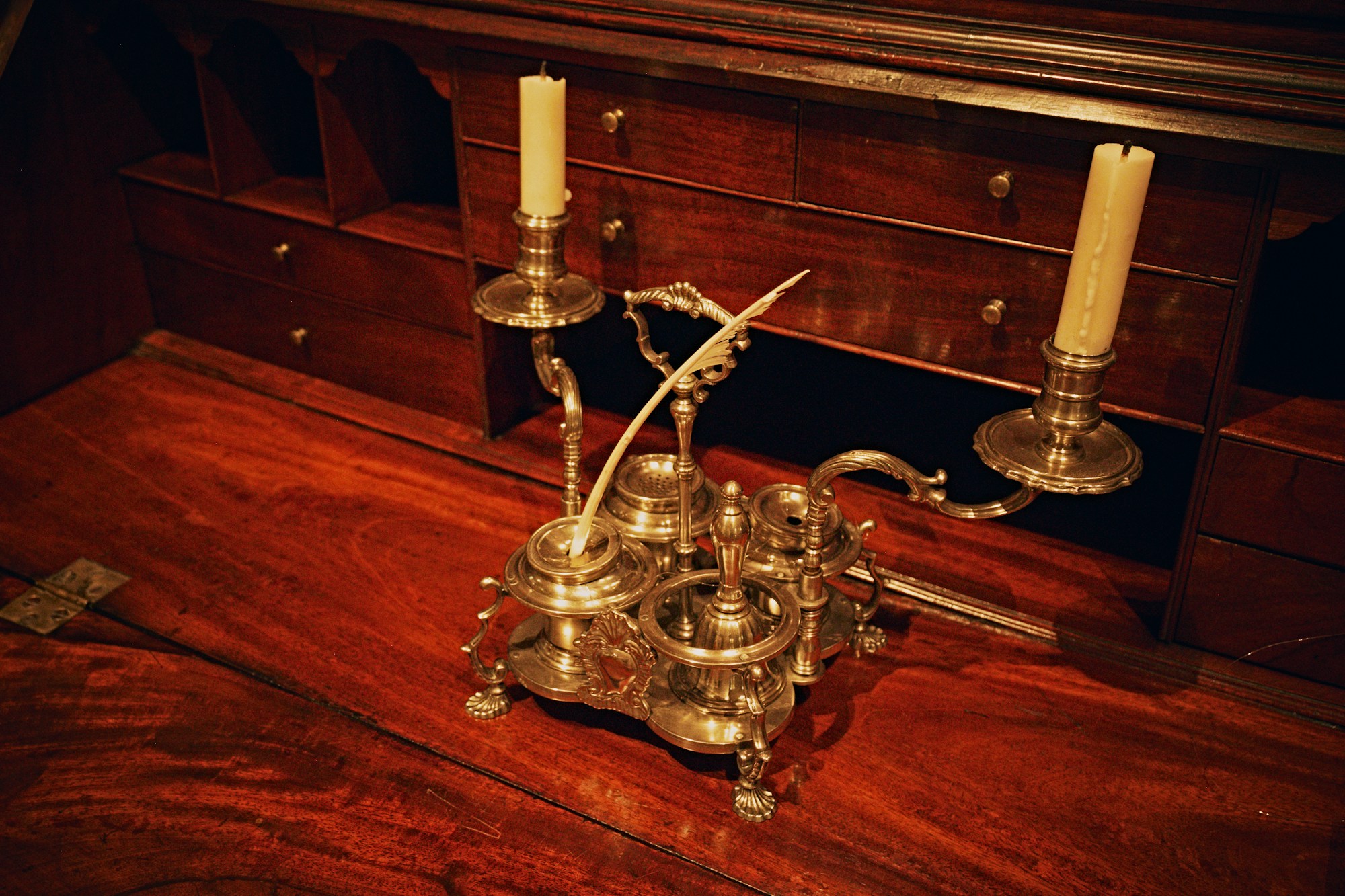 A polished antique brass inkwell set with two candlesticks on a wooden desk