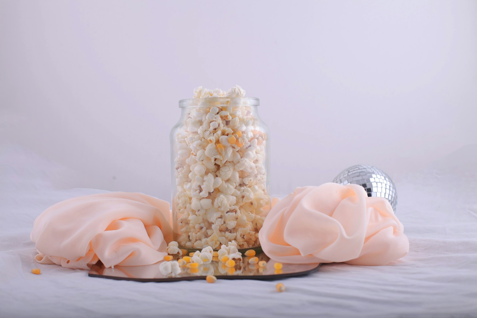 A glass jar filled with fluffy popcorn on a soft pink cloth