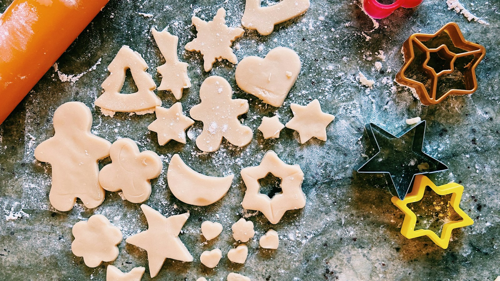 Salt dough stars, hearts, trees and gingerbread shapes cut with metal cookie cutters on a floured counter