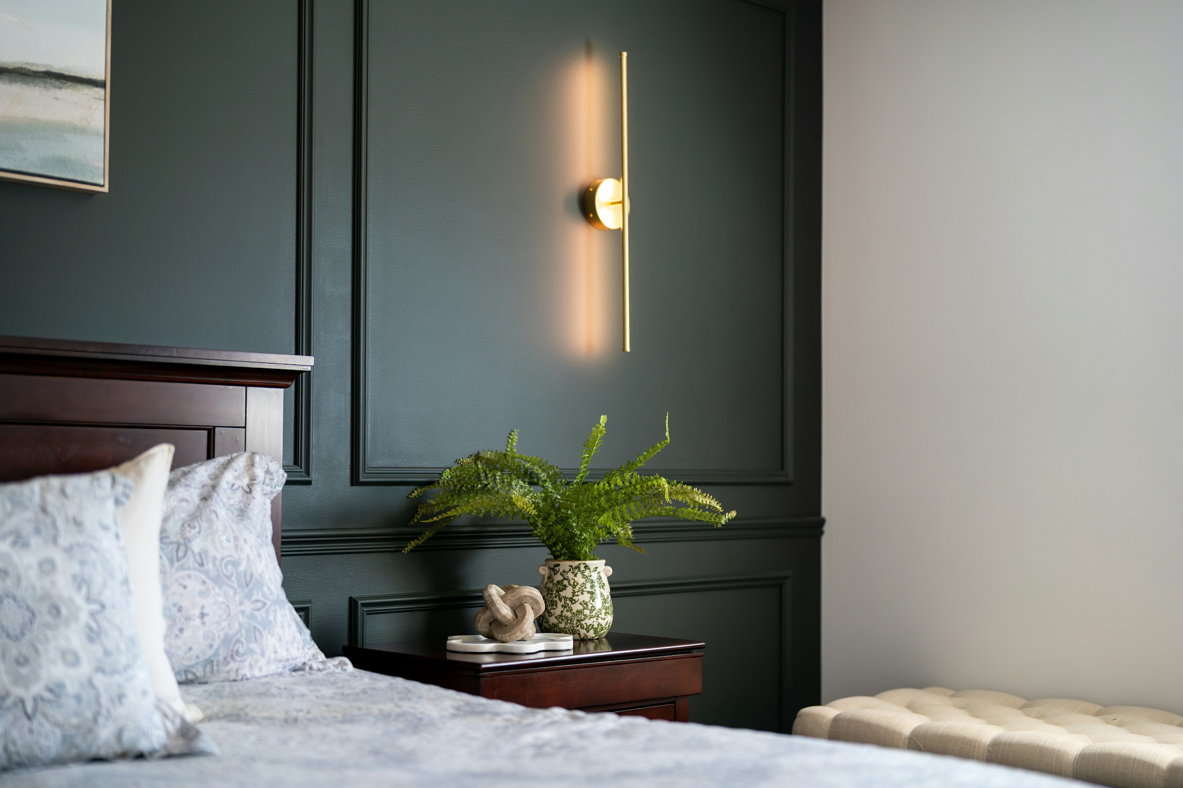 Bedroom with a dark green wall and a stylish wall light beside the bed