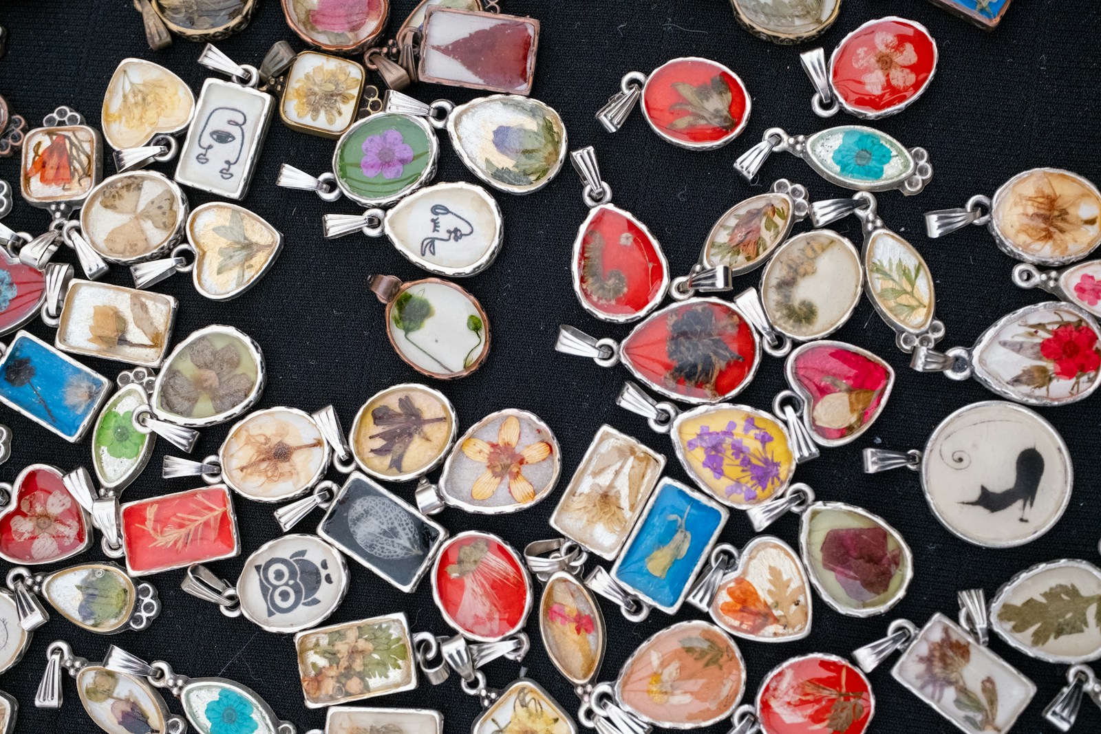 Epoxy resin creations: many handmade resin pendants with dried flowers on a dark cloth