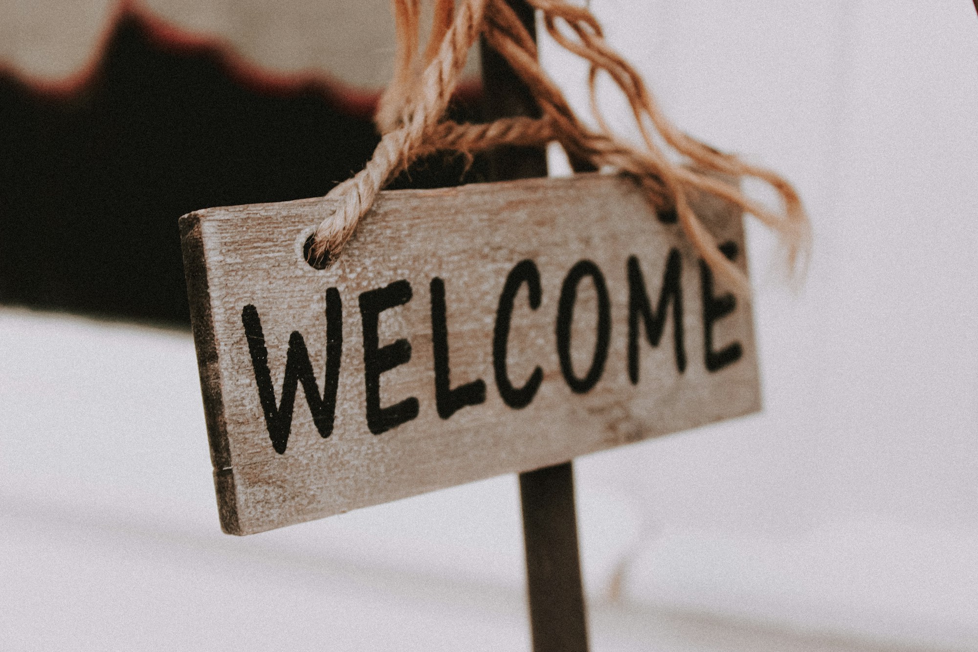 A rustic wooden plank welcome sign hanging from a thick rope