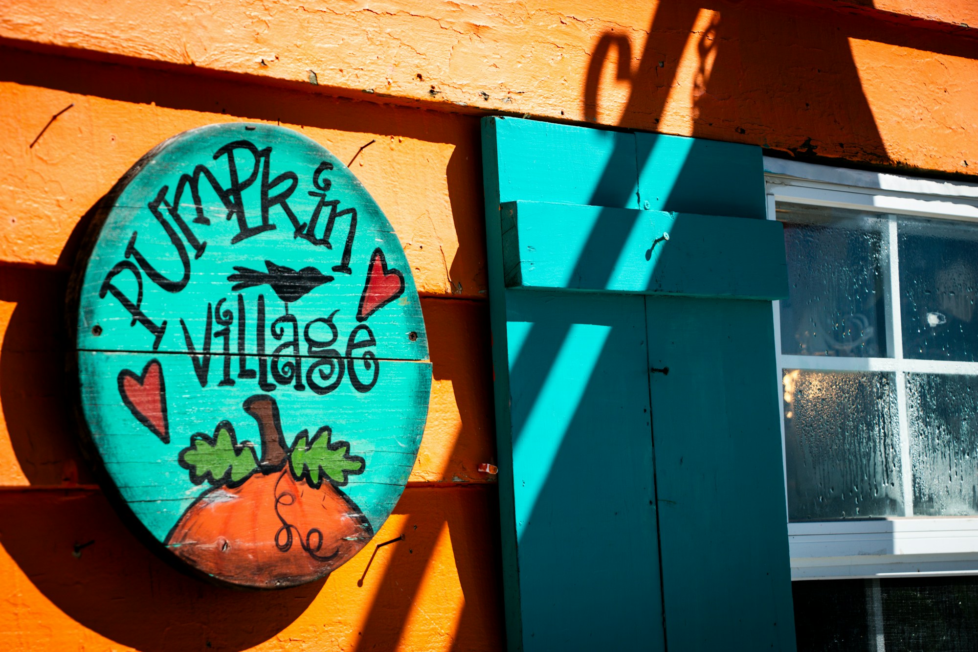 DIY front door signs inspiration: a round turquoise folk art sign painted with a pumpkin and hearts