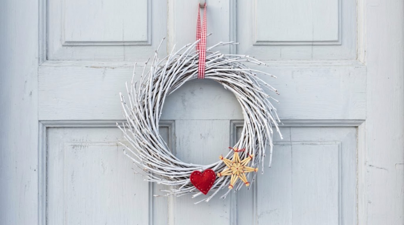 Scandinavian Christmas decor: white painted twig wreath with a red felt heart and straw star on a grey door