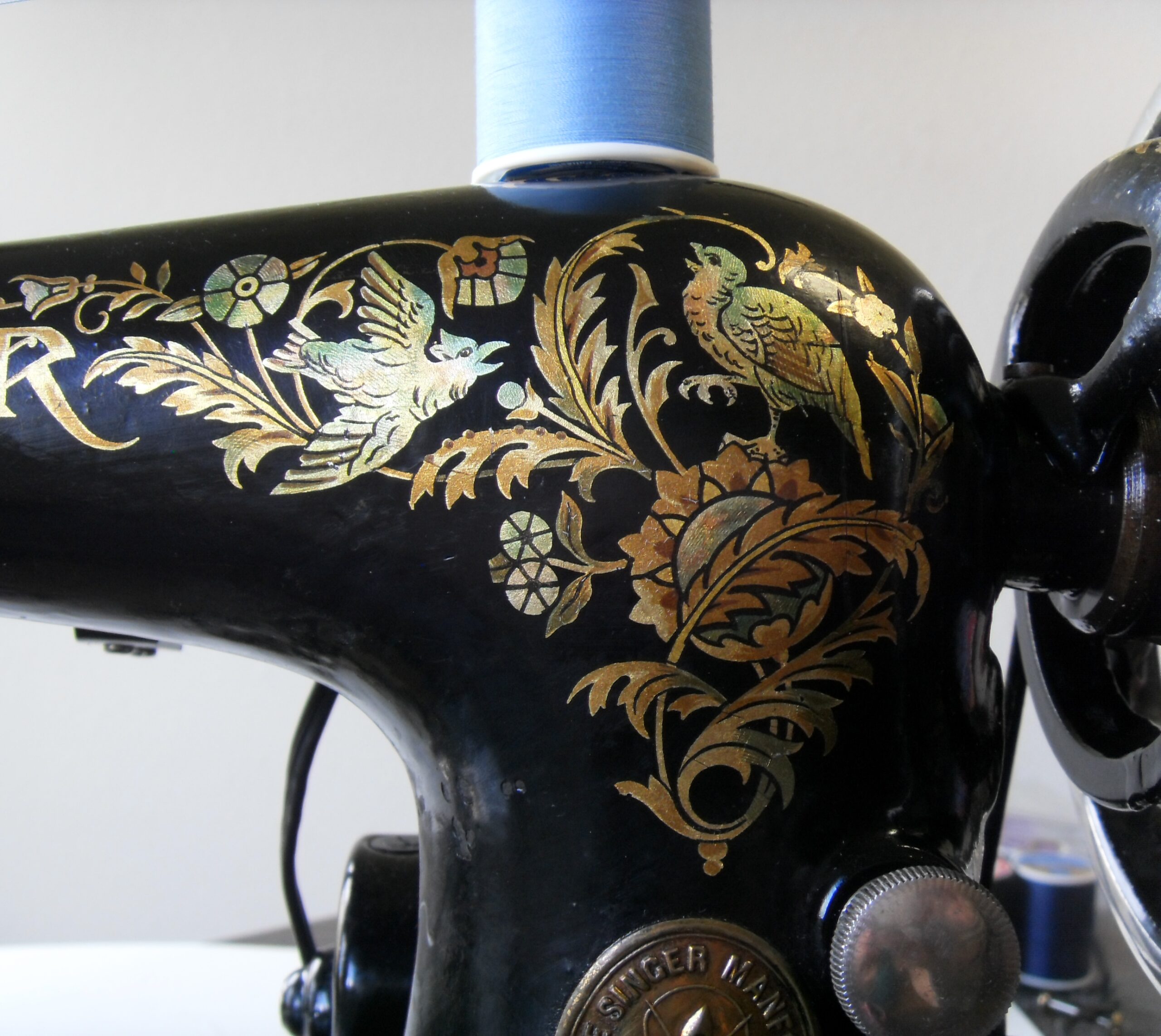 Close view of an ornate gold bird and leaf decal on an antique black sewing machine