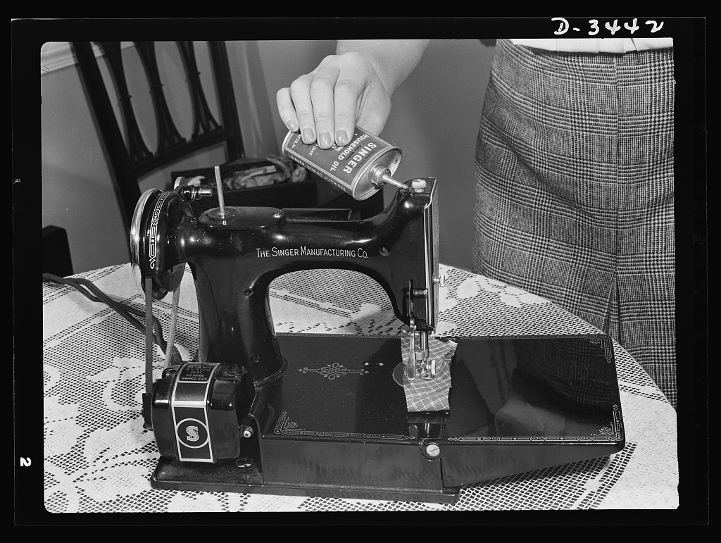 Black and white photo of a hand oiling a vintage electric sewing machine