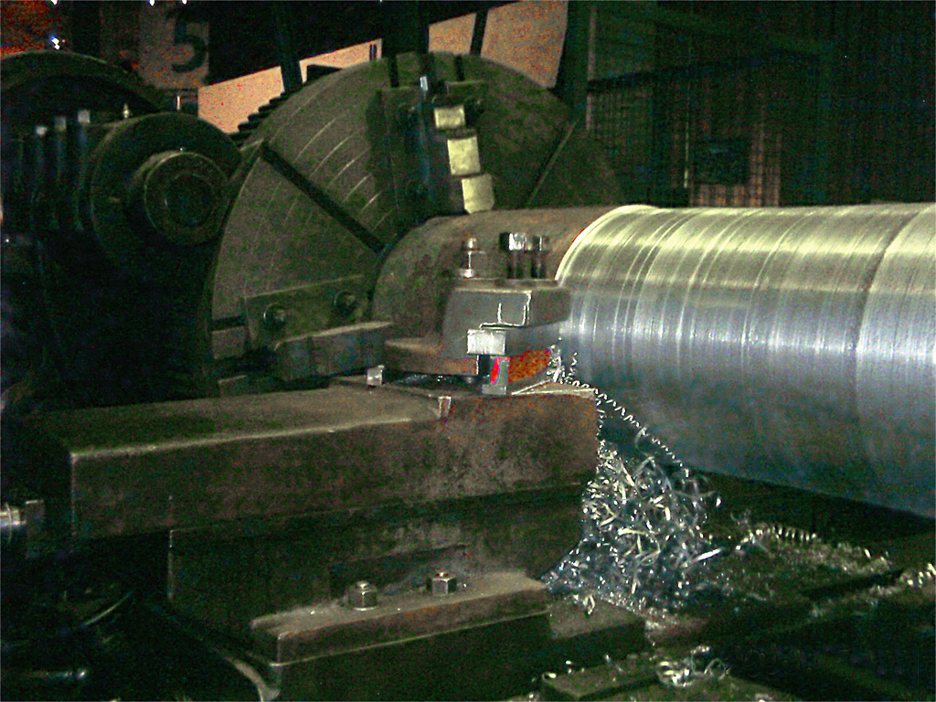 A metal lathe cutting a shiny steel part with curly metal shavings
