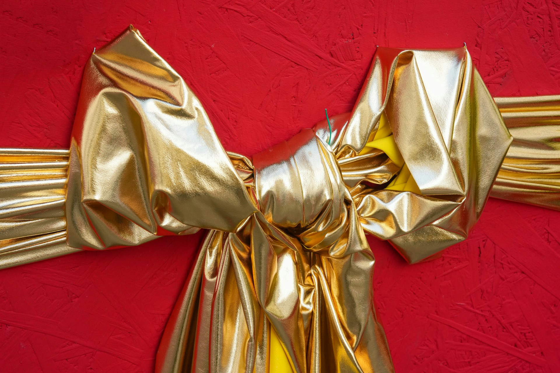 Big shiny gold fabric bow on a red background