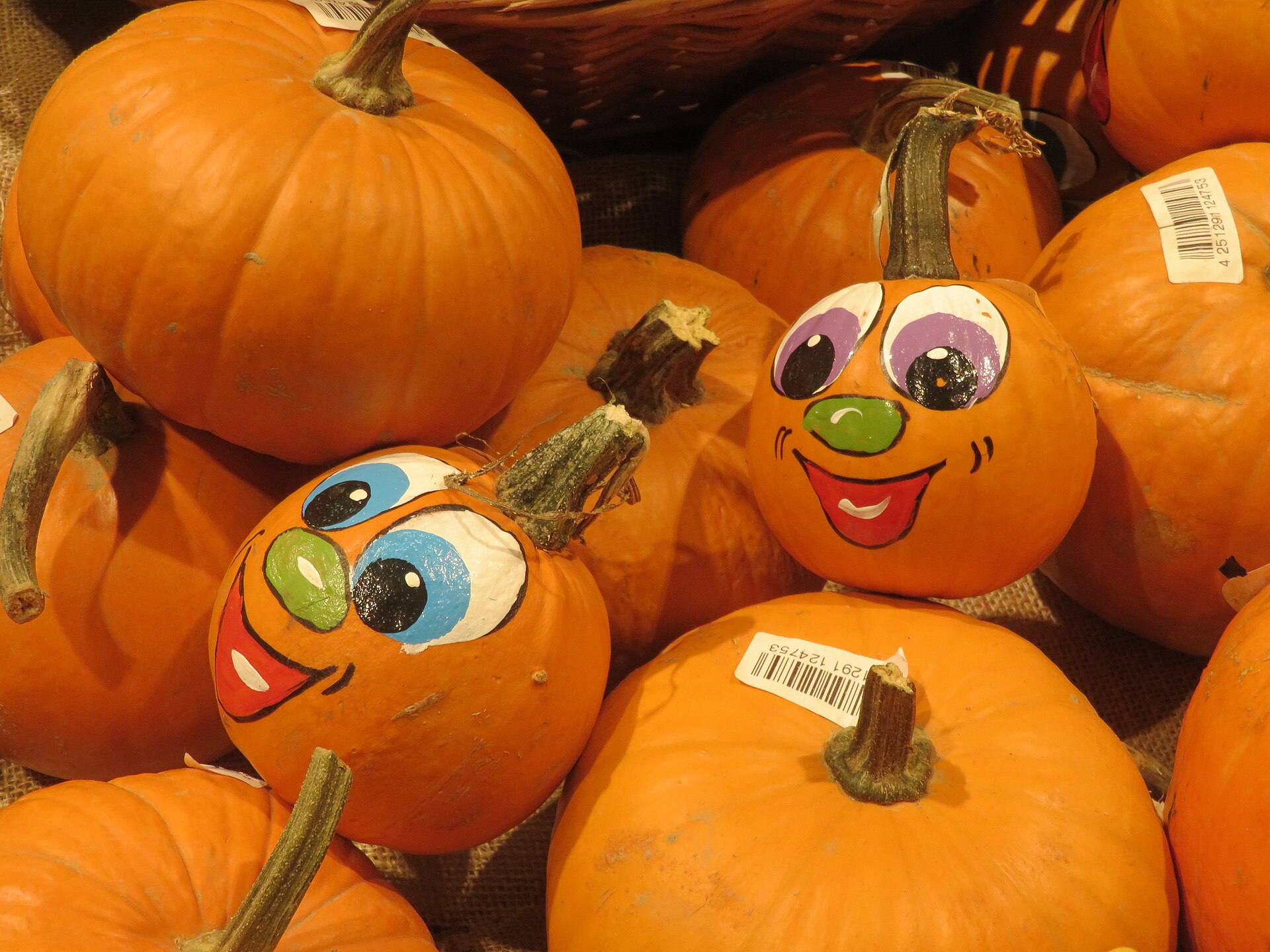 A pile of orange pumpkins with hand painted silly faces