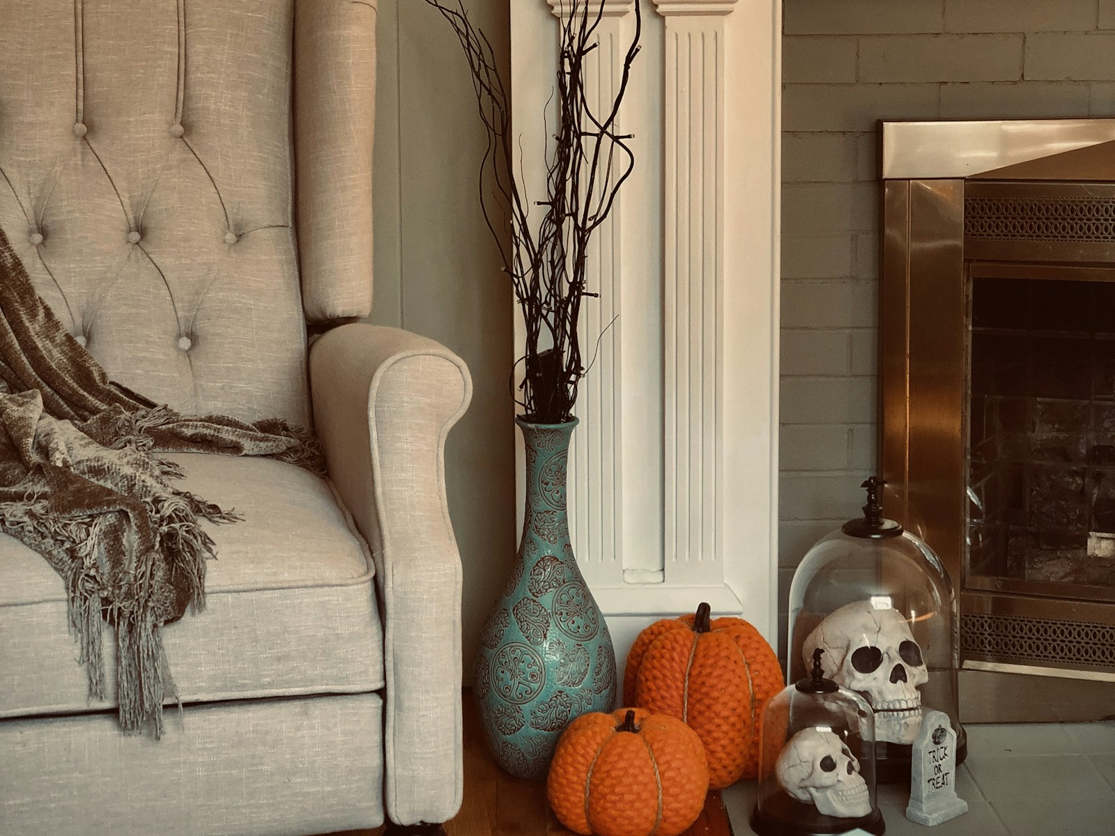 Skulls under a glass cloche beside orange pumpkins and black branches by a white fireplace