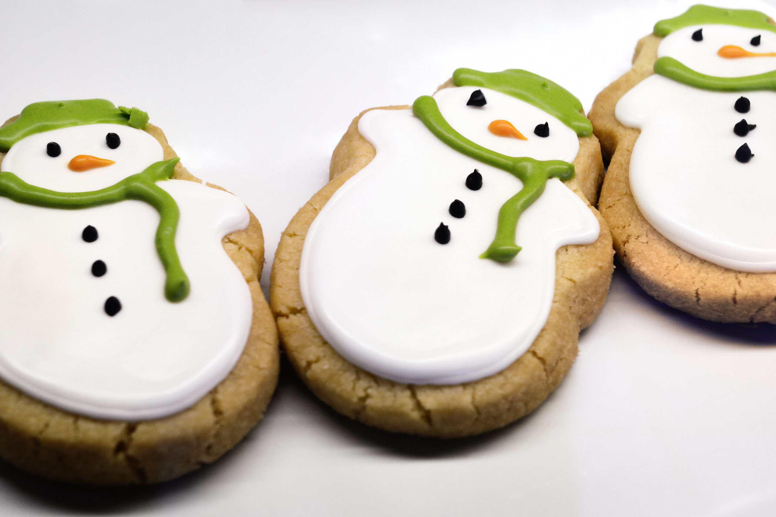 Snowman shaped sugar cookies decorated with white icing and colorful scarves