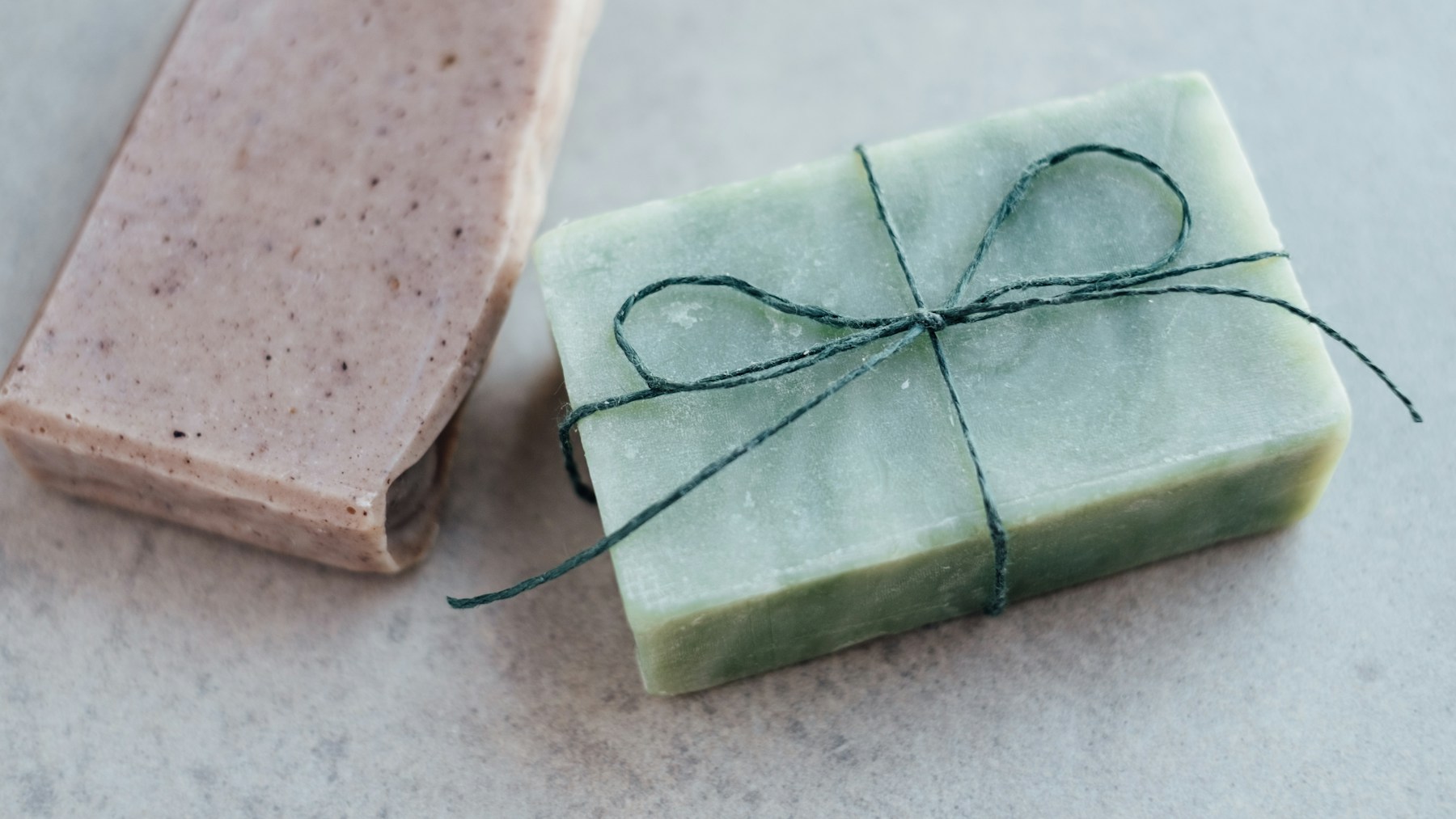 Pale green handmade soap bar tied with dark green string on a gray table
