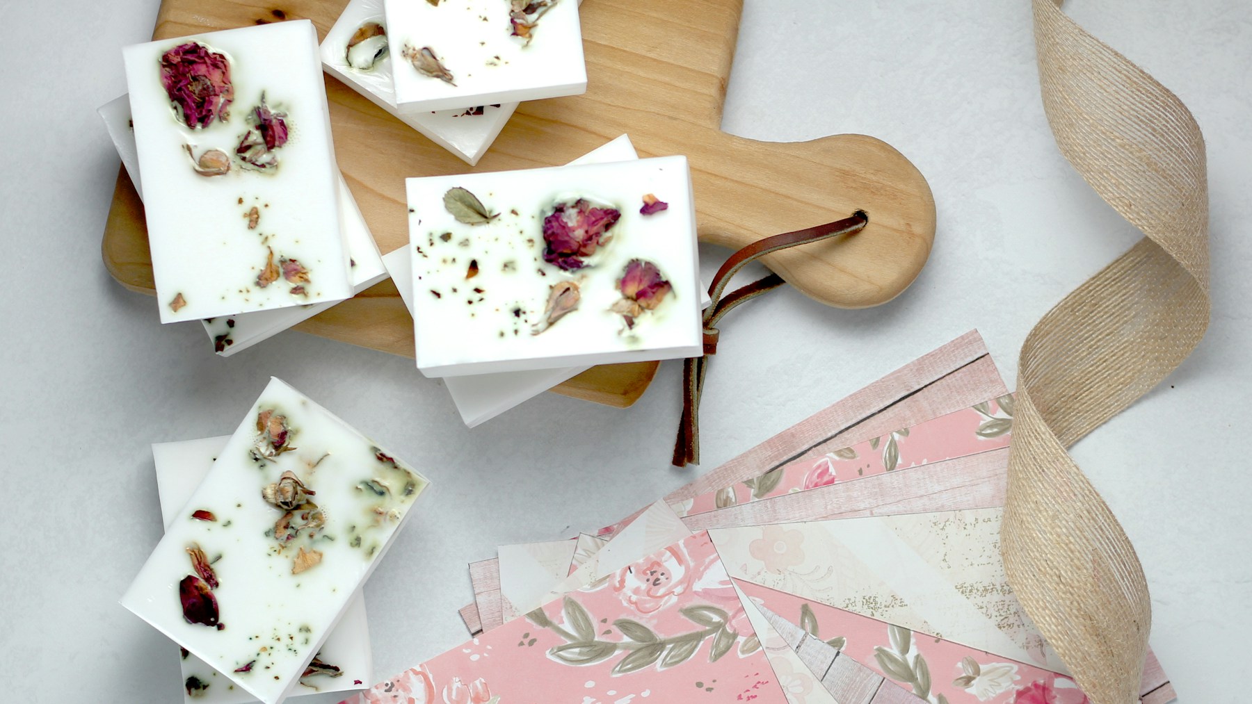 White soap bars topped with dried flowers on a wooden board with floral paper