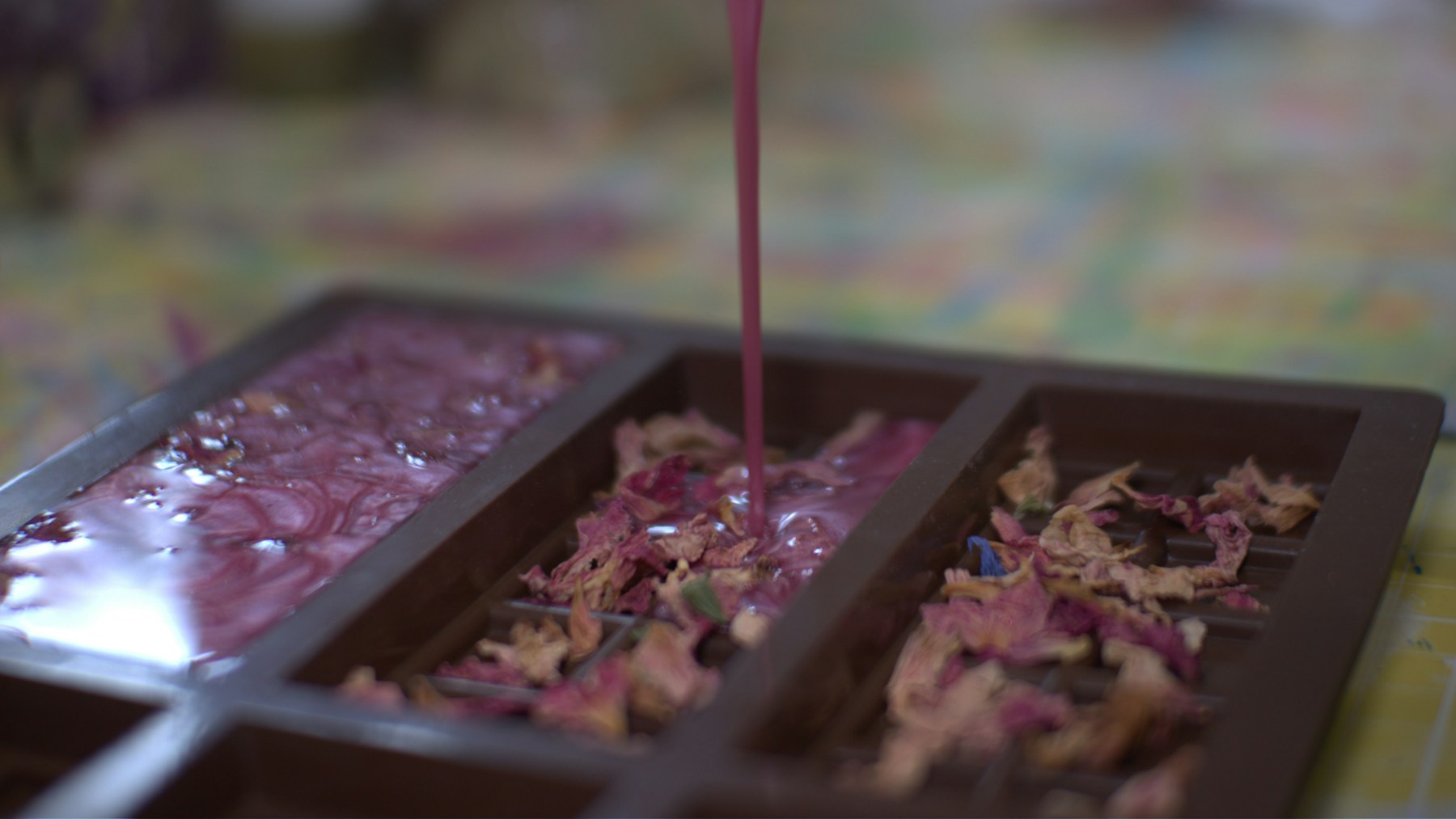 Pink melt and pour soap being poured into a silicone mold with dried rose petals