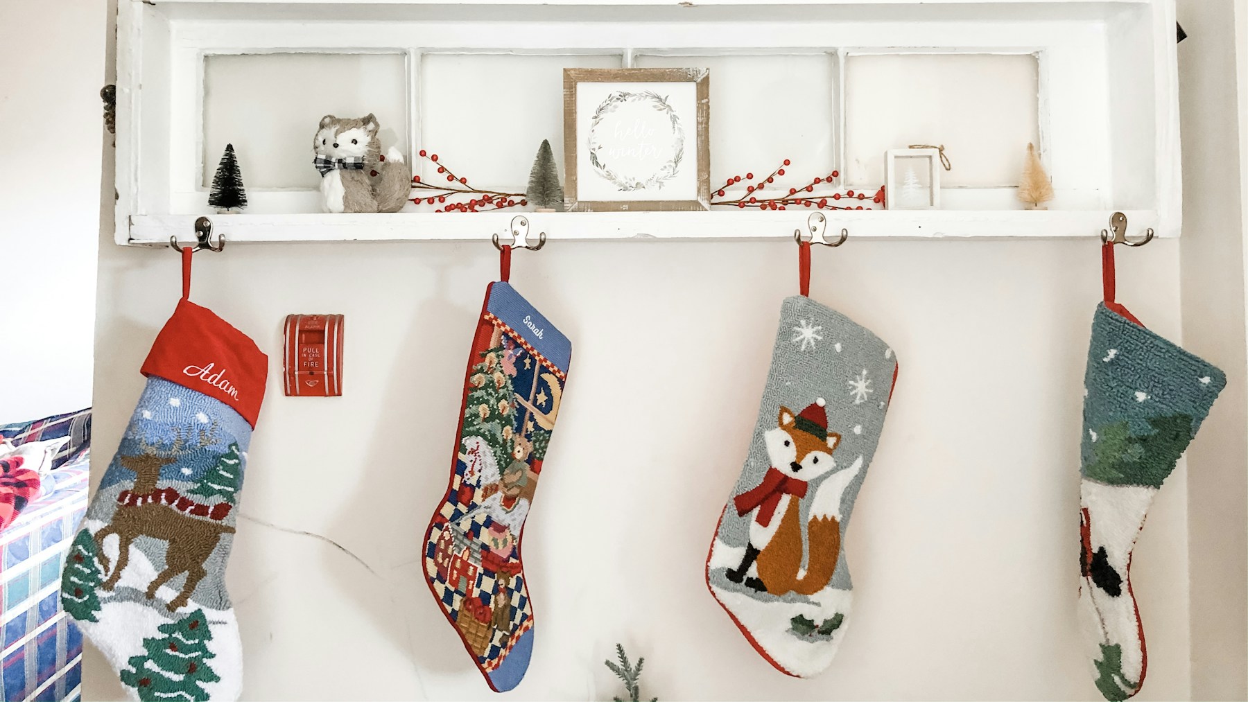 Needlepoint Christmas stockings hanging from hooks under a white wall shelf