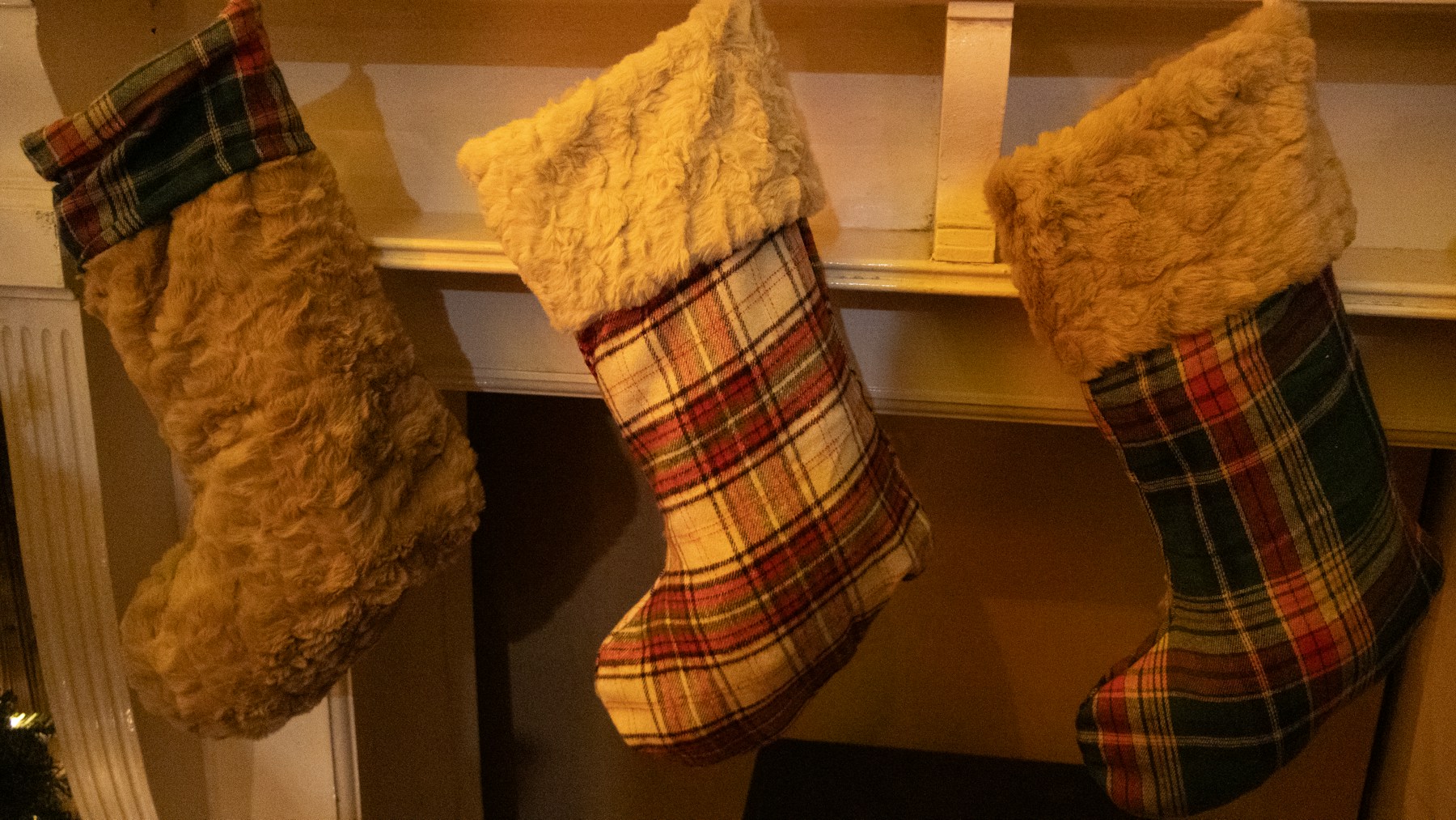 Plaid flannel and faux fur Christmas stockings hanging on a wood mantel