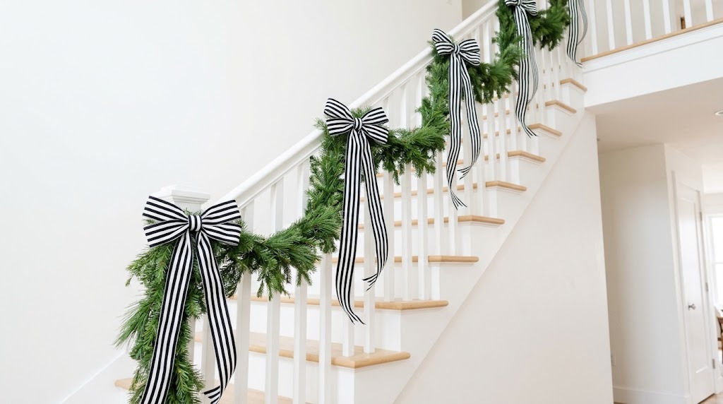 Black and white striped ribbon bows tied along a pine garland on a white staircase banister