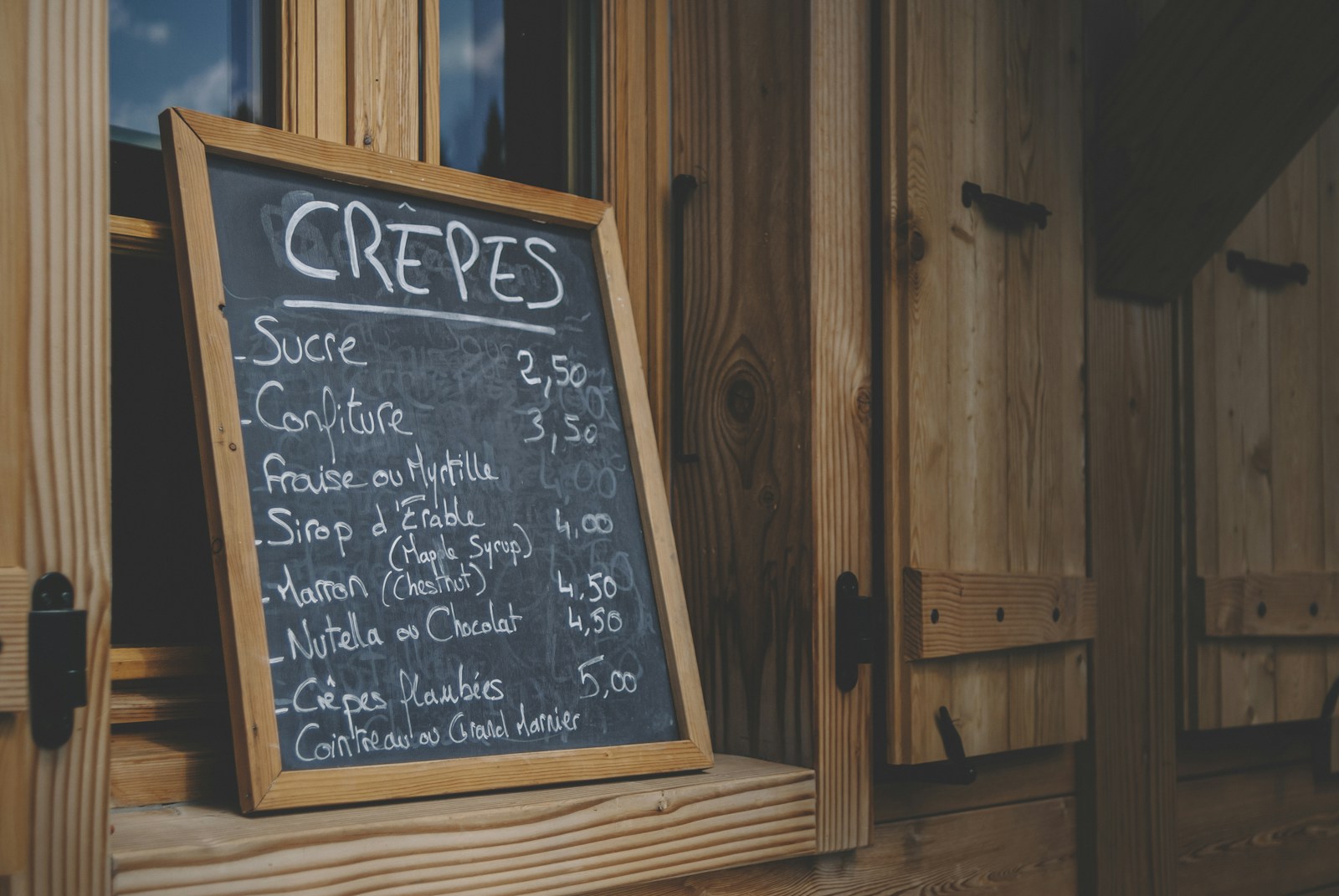 A hand lettered chalkboard menu in a wooden frame on a wood wall