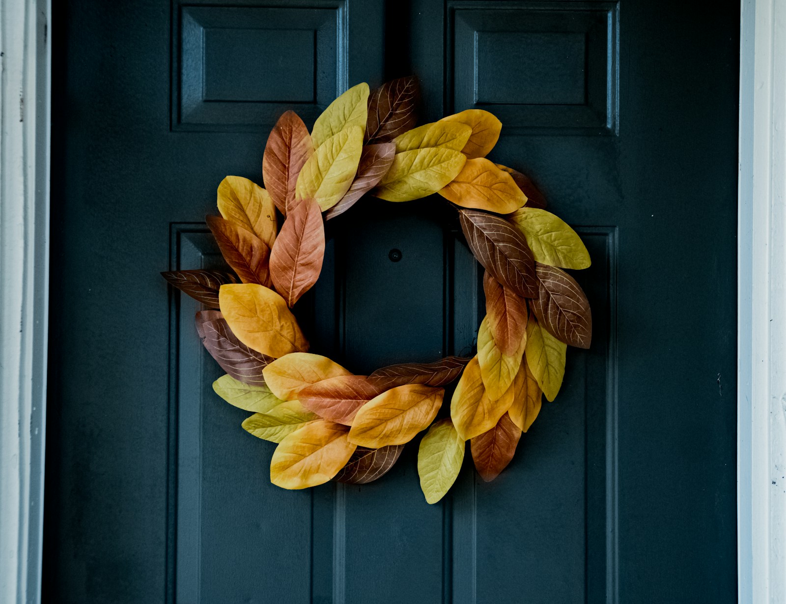 A wreath of dried golden leaves hanging on a dark blue front door