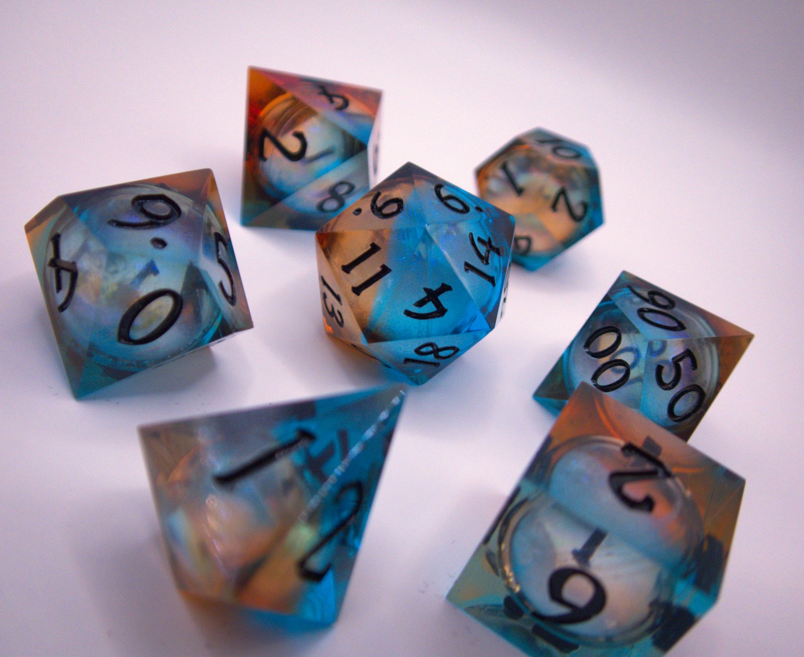 Translucent blue and orange polyhedral dice scattered on a white surface