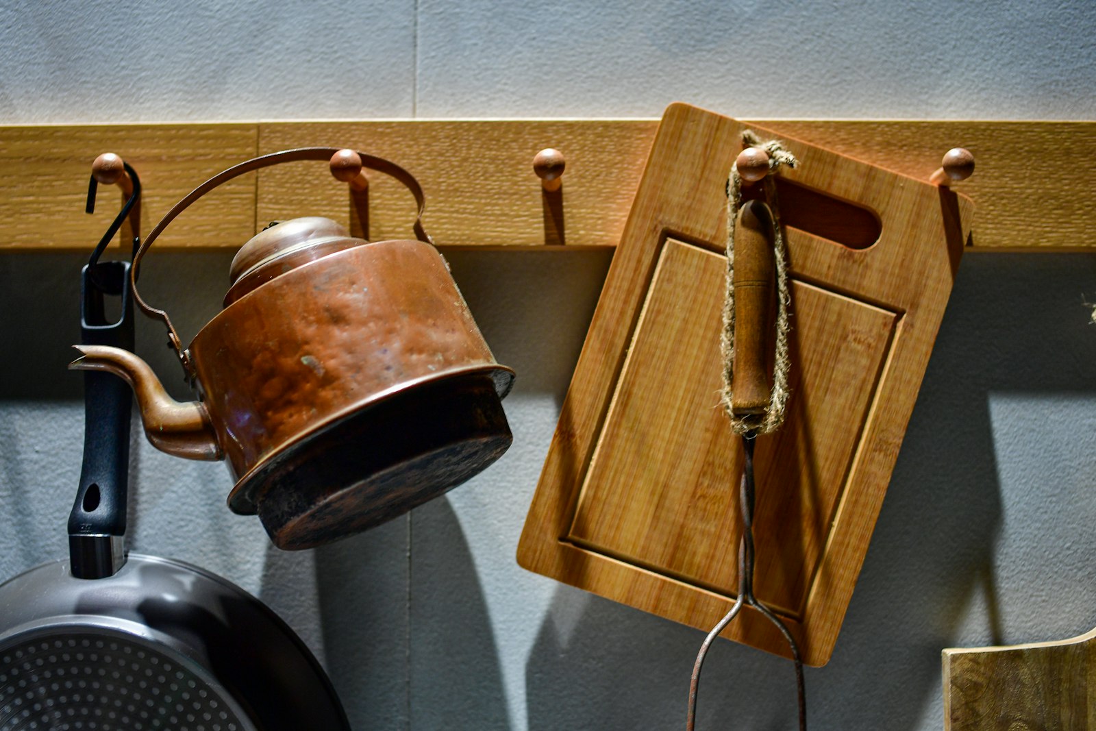 Old copper kettle and a wooden board hanging from pegs on a kitchen wall