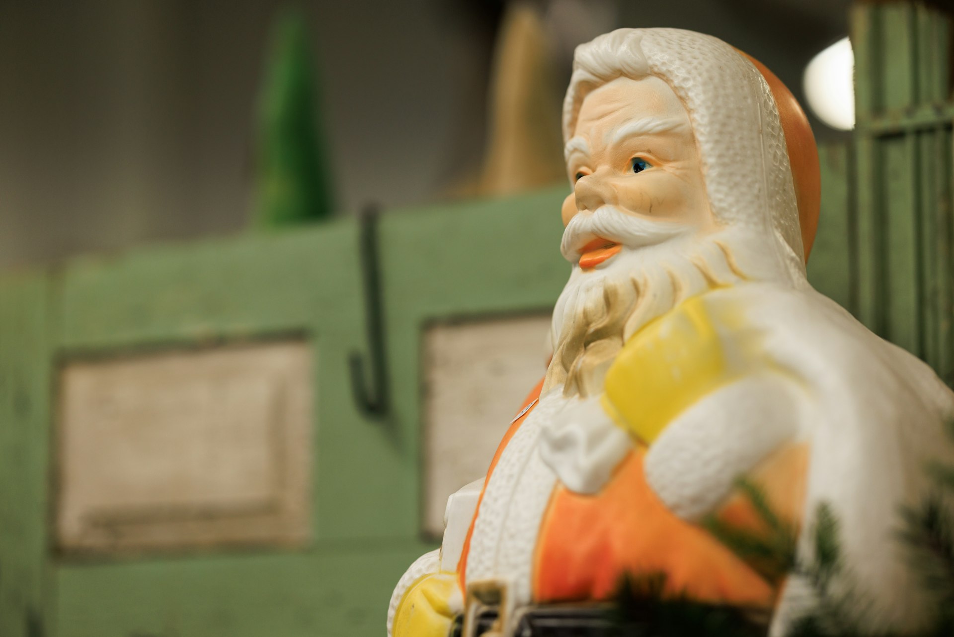 Close view of a vintage plastic Santa blow mold with a green wall behind it