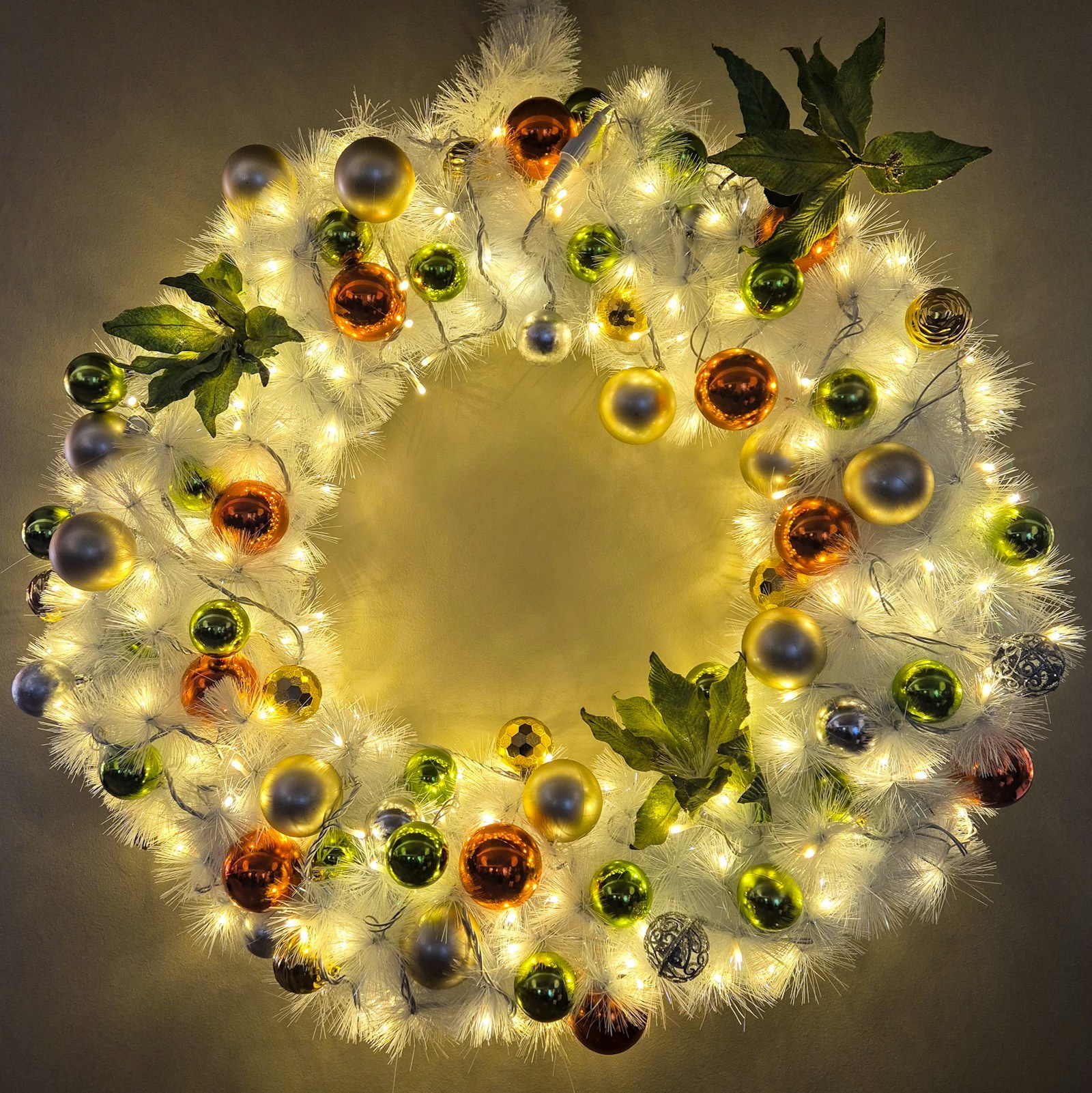 Round wreath packed with shiny ornaments in many colors and glowing fairy lights