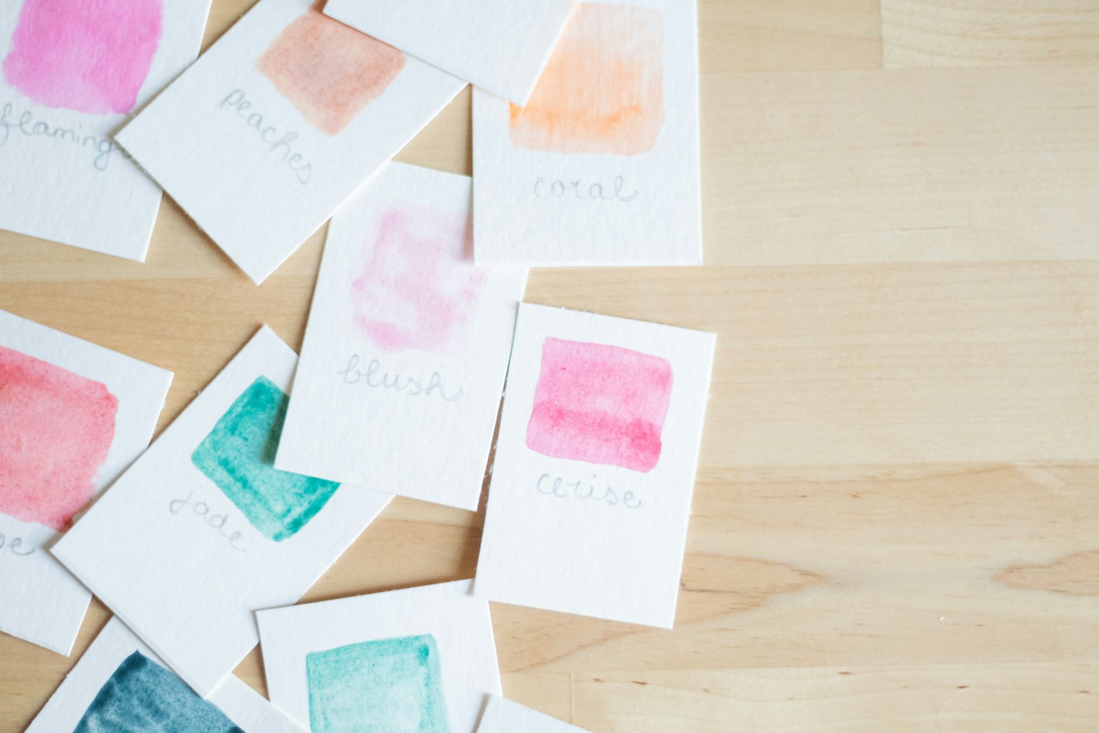 Small hand painted watercolor cards scattered on a wooden table