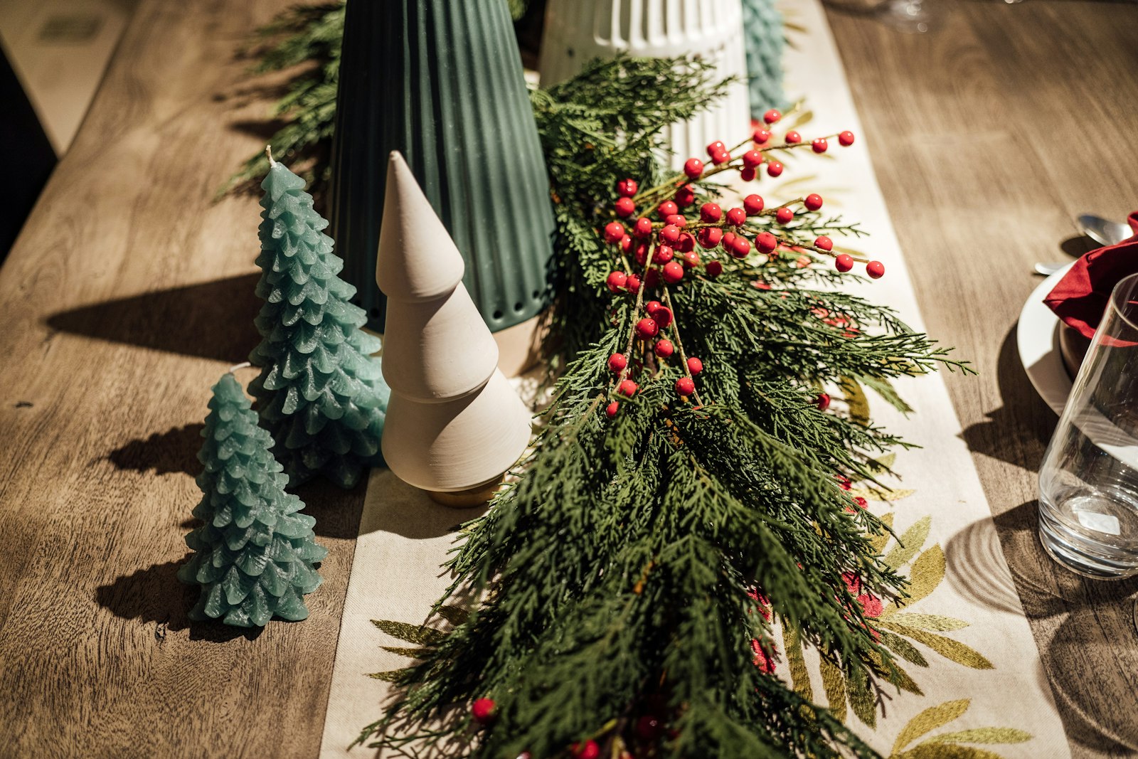 Woodland Christmas decor on a dining table: a cedar and berry runner with small ceramic trees