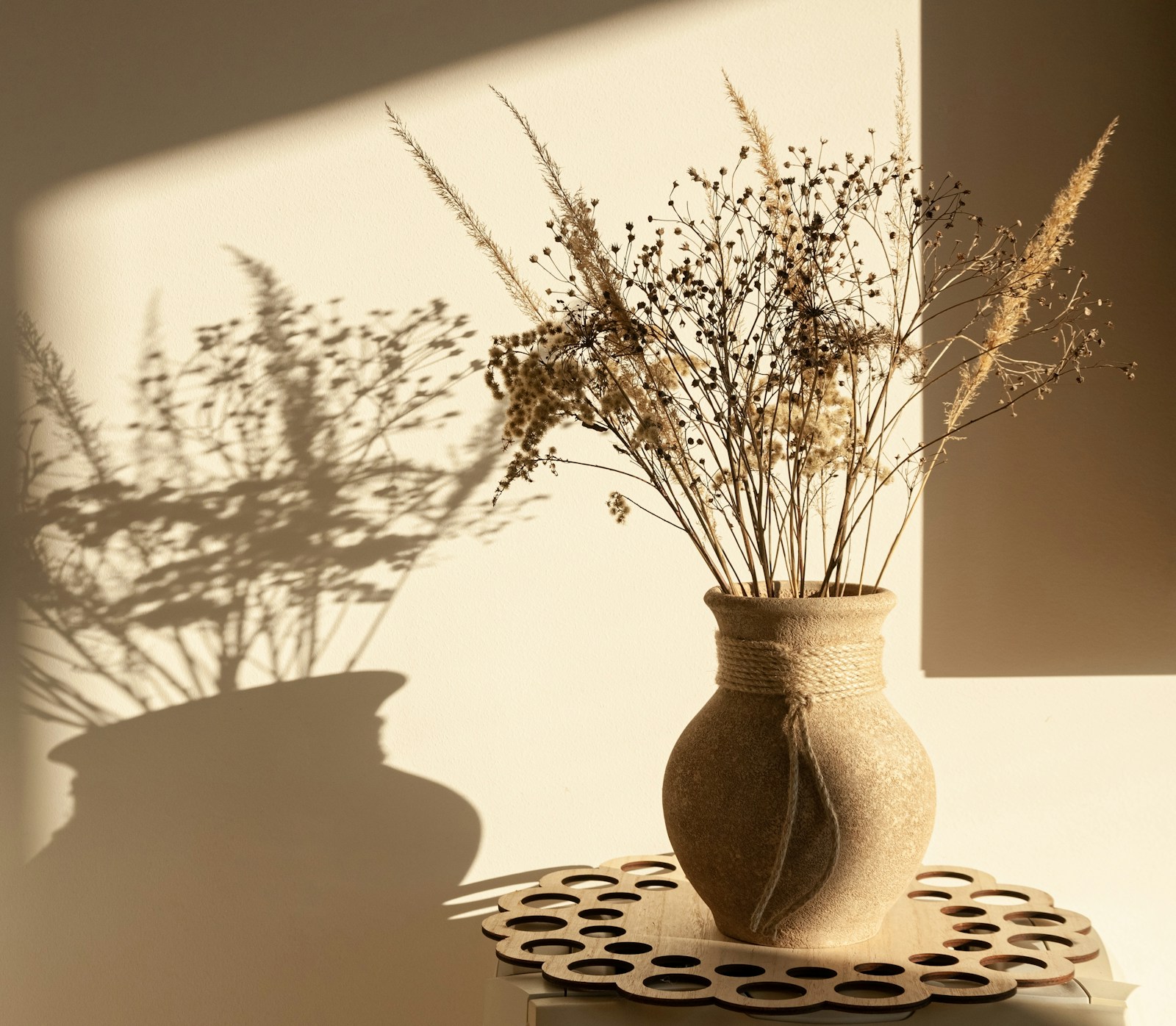 Dried grasses and flowers in a rustic clay vase casting soft shadows