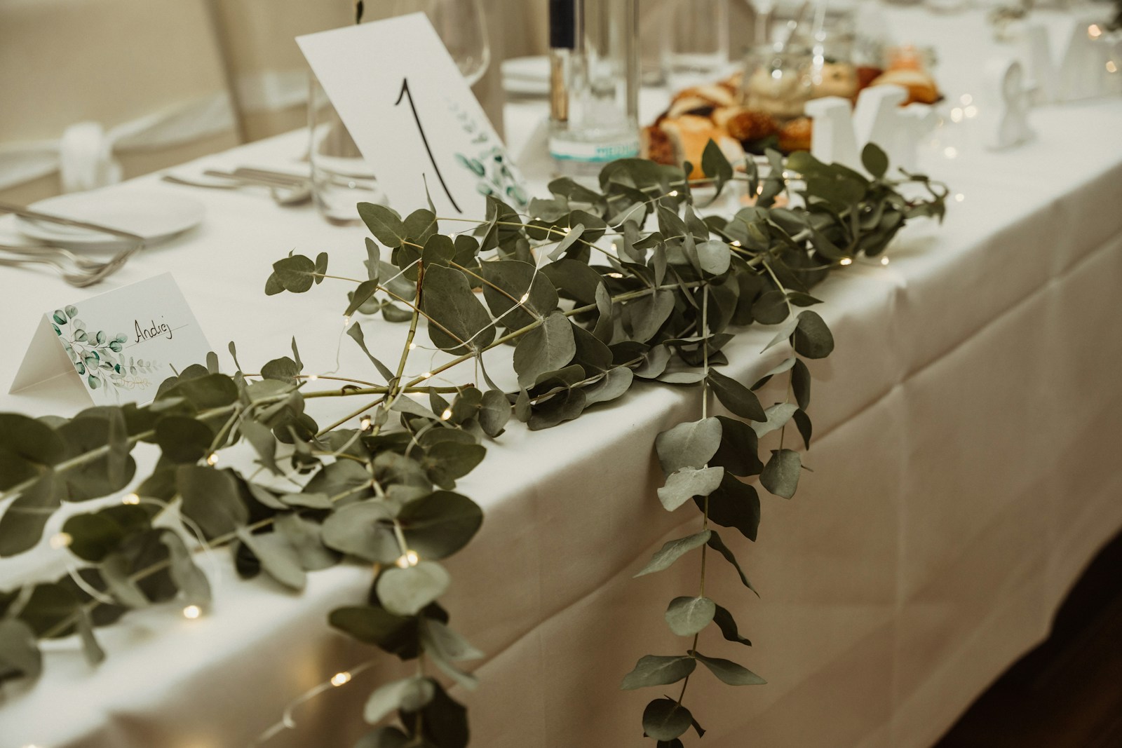 A loose eucalyptus garland running down a white wedding tablecloth