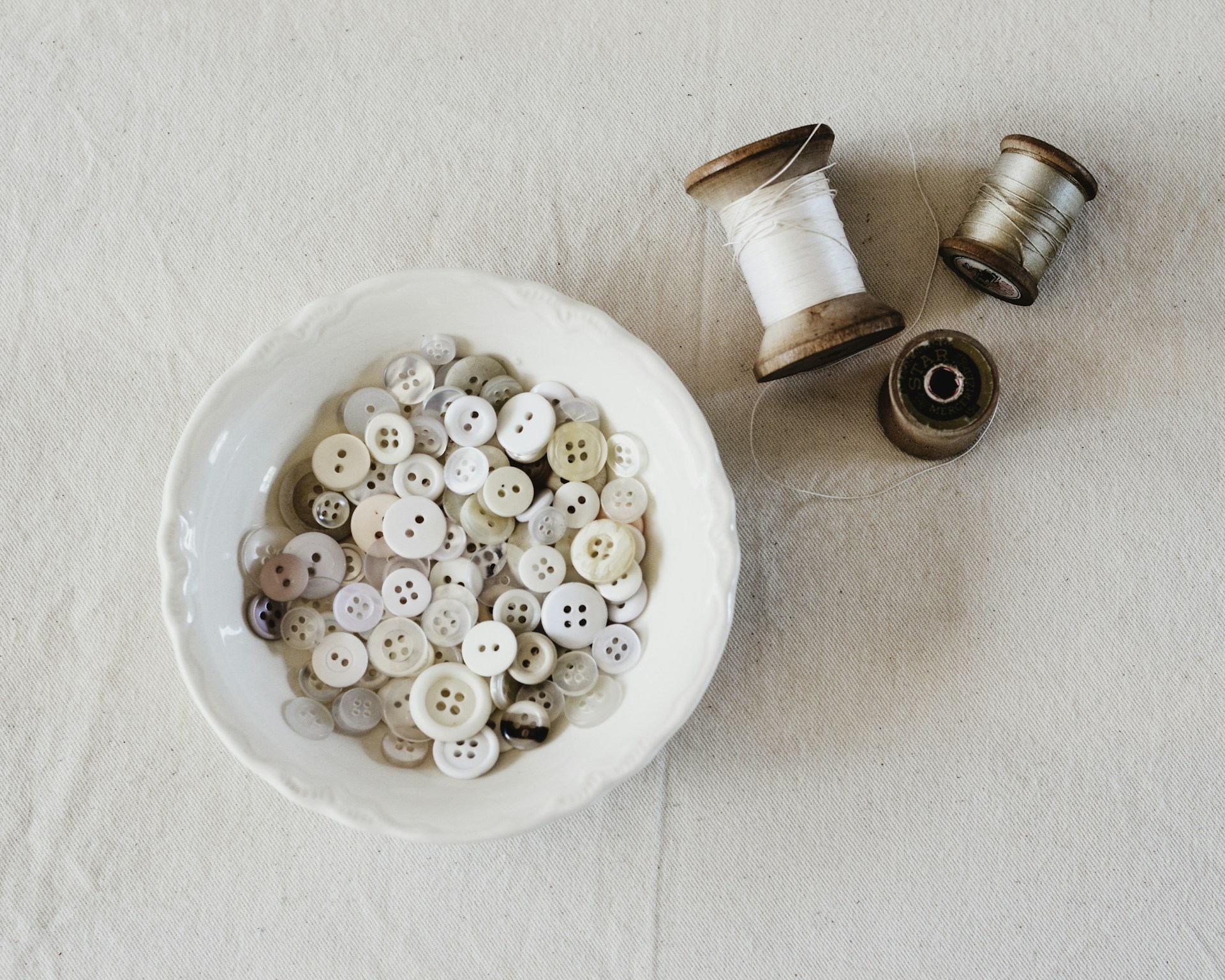 White bowl filled with vintage buttons next to spools of thread