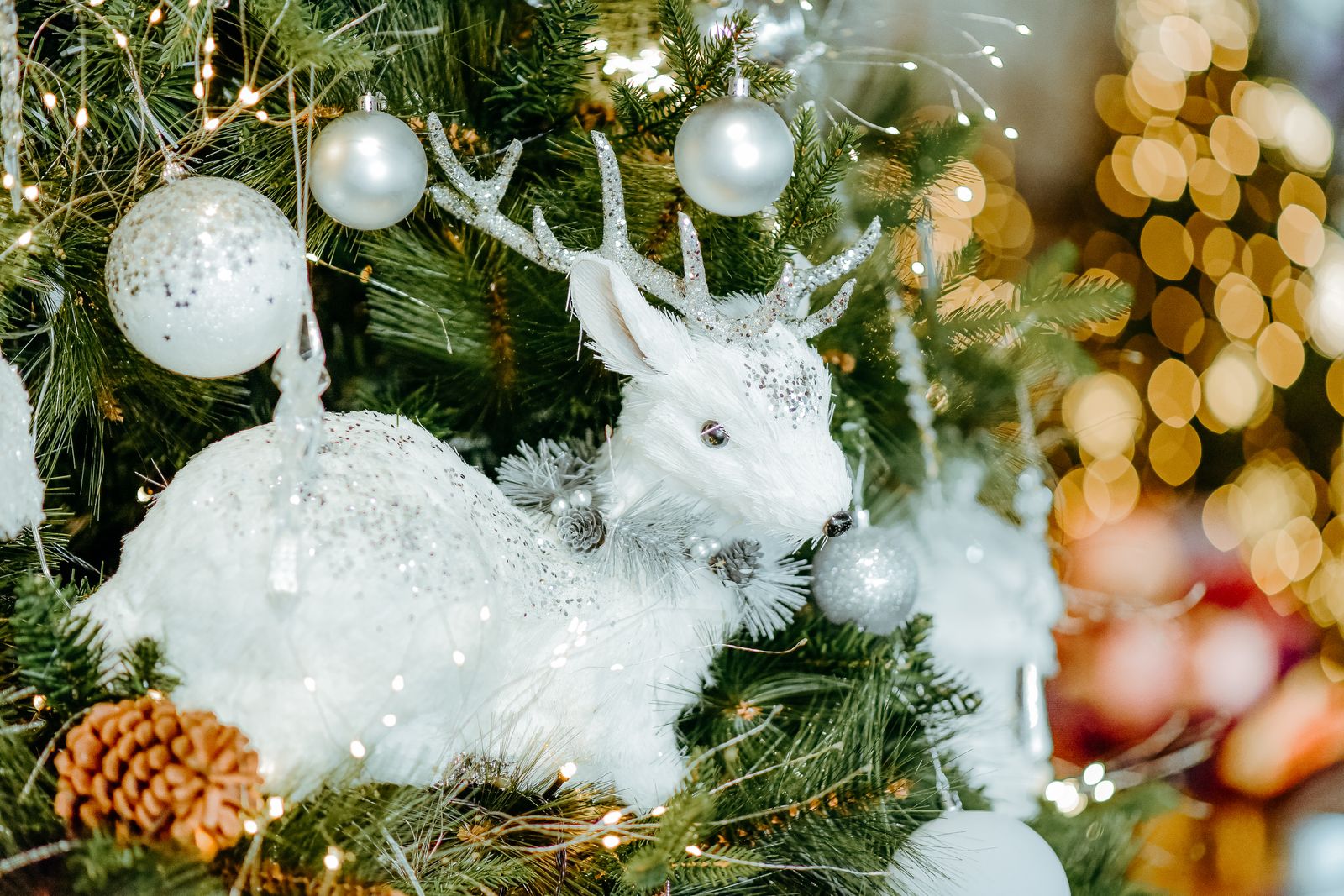 A white deer figure and silver ornaments tucked into a Christmas tree