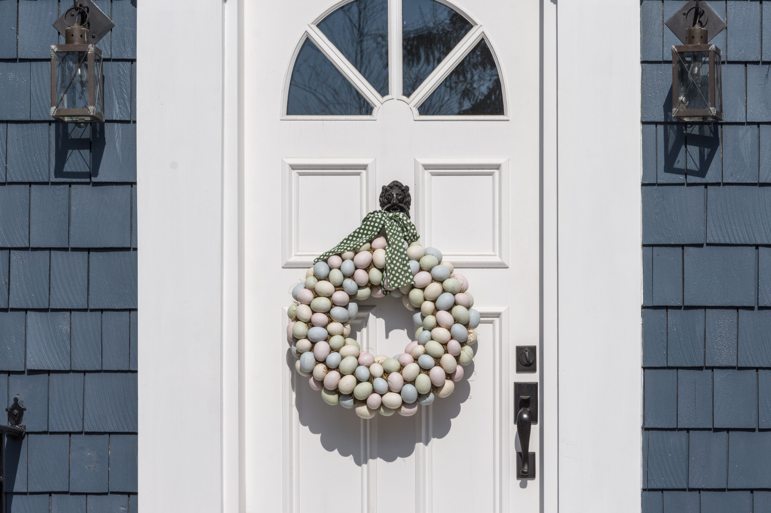A white front door with a round wreath between two lanterns