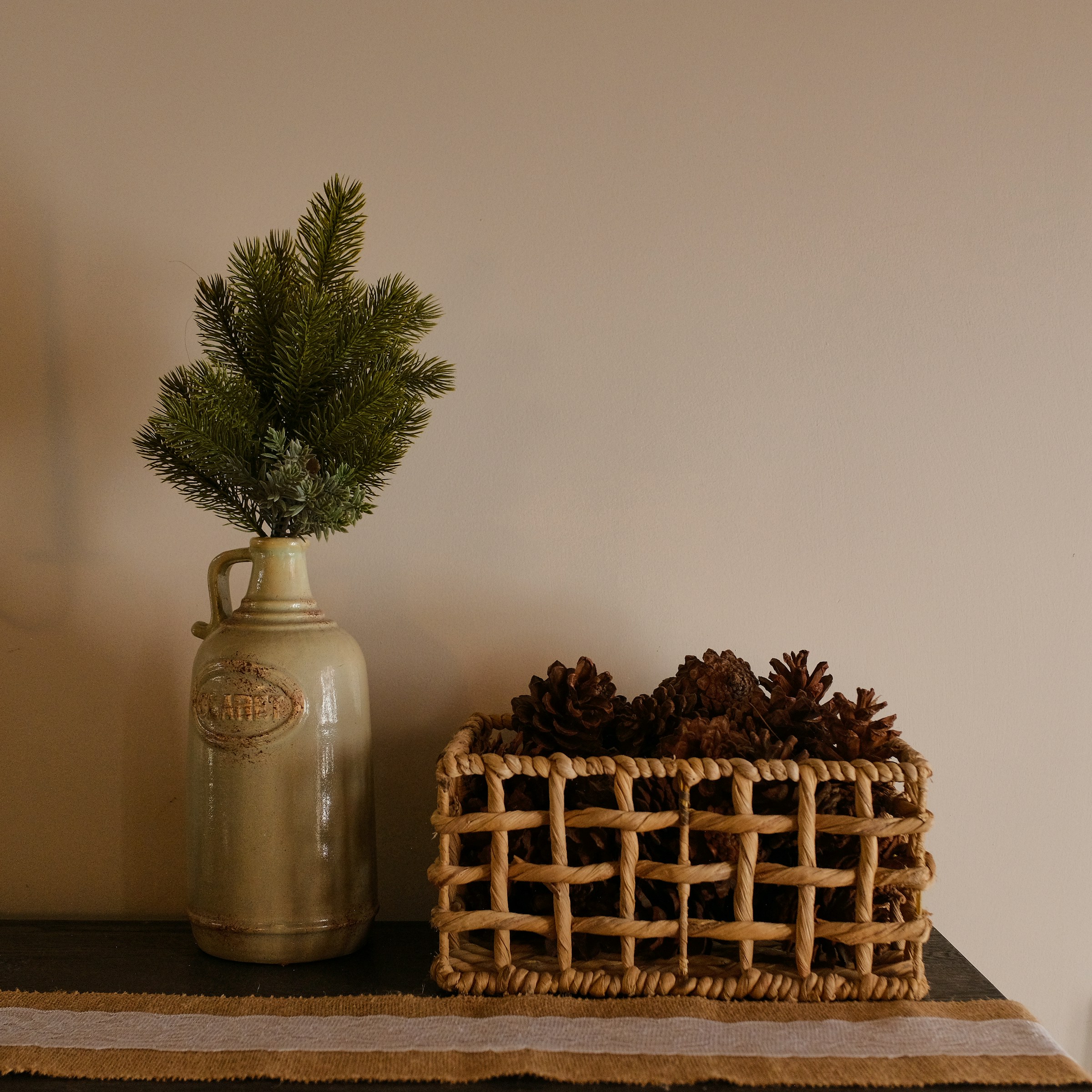 Pine sprig in a small jug next to a basket of pinecones