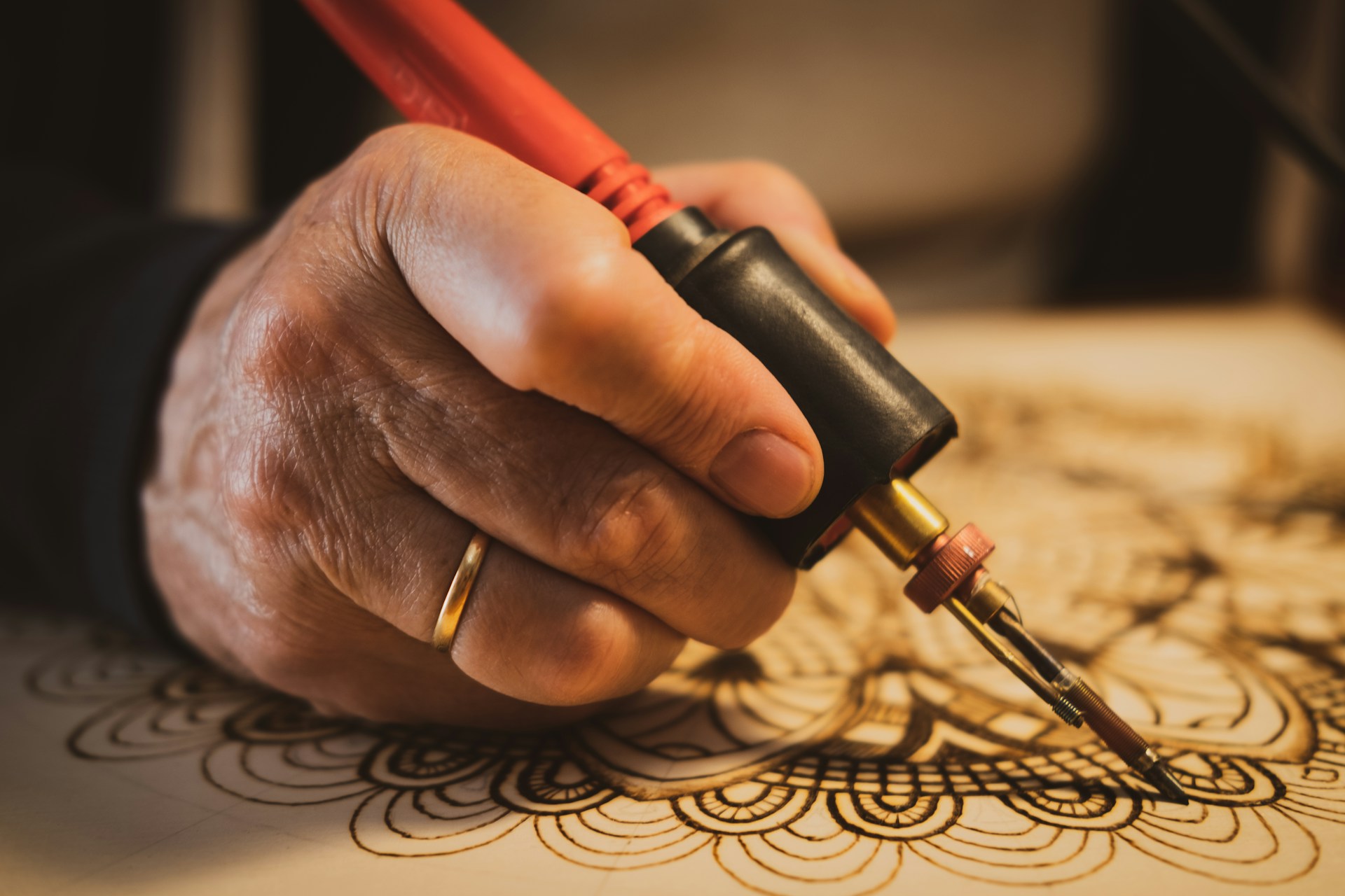 Wood burning art mandala pattern of circles and petals being traced on a pale wood board