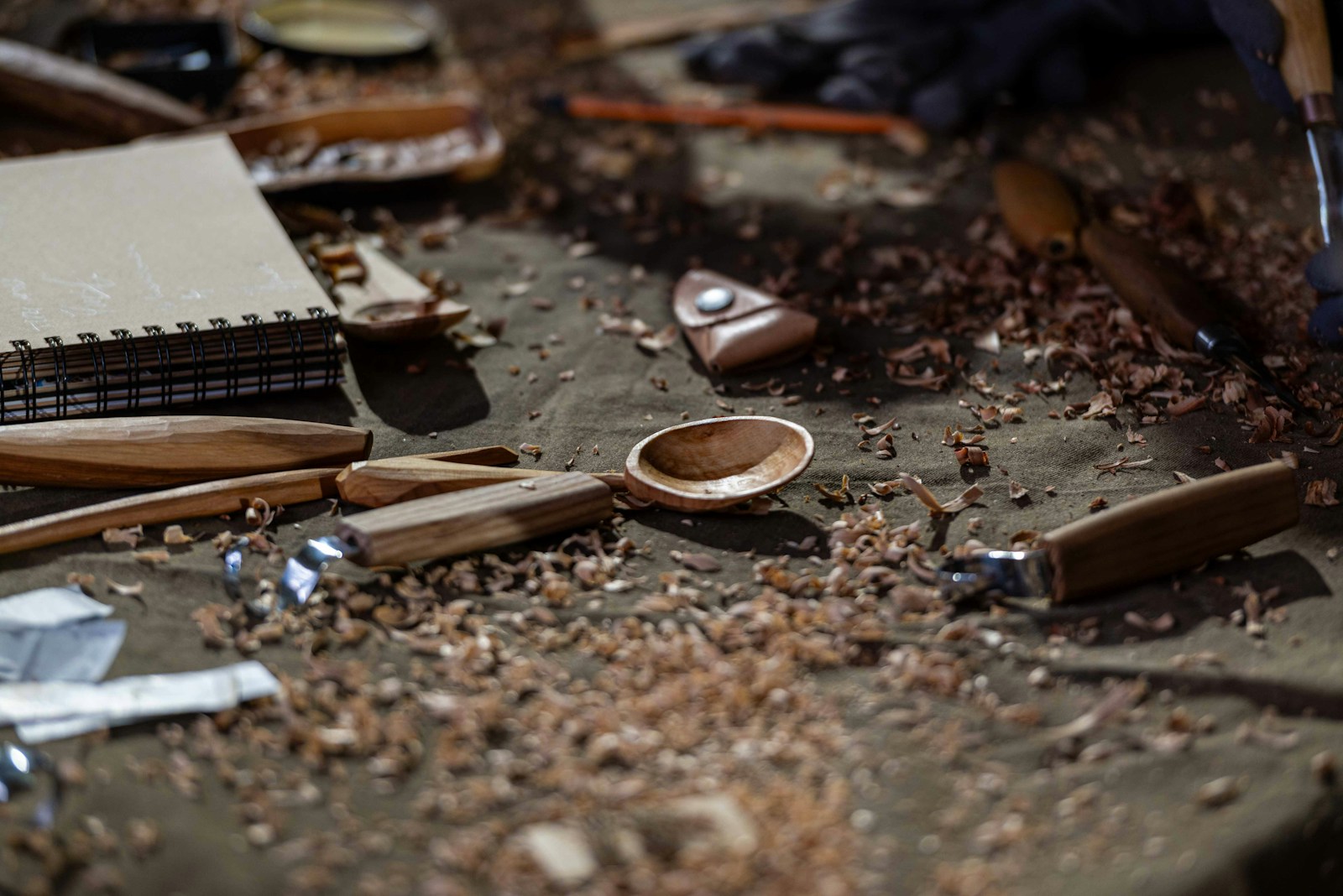 Carving tools and fresh shavings on a workbench next to a small spoon