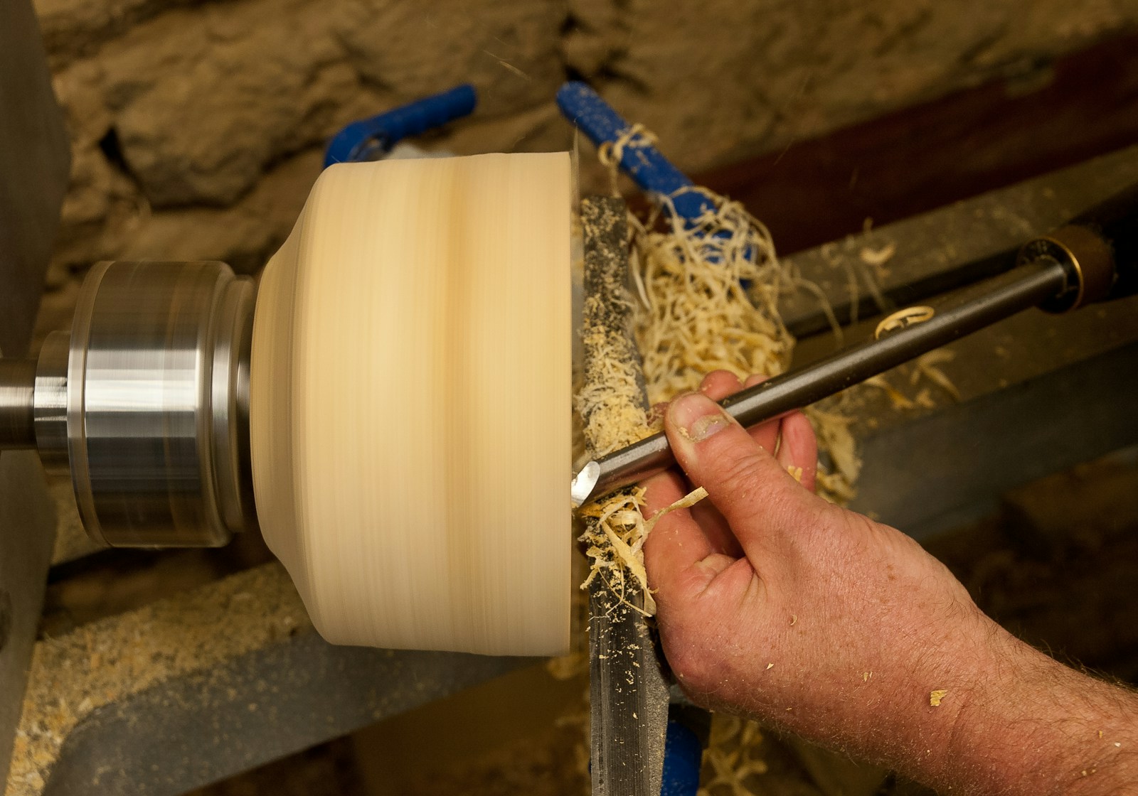 Woodturner shaping a round blank on a lathe with a long gouge