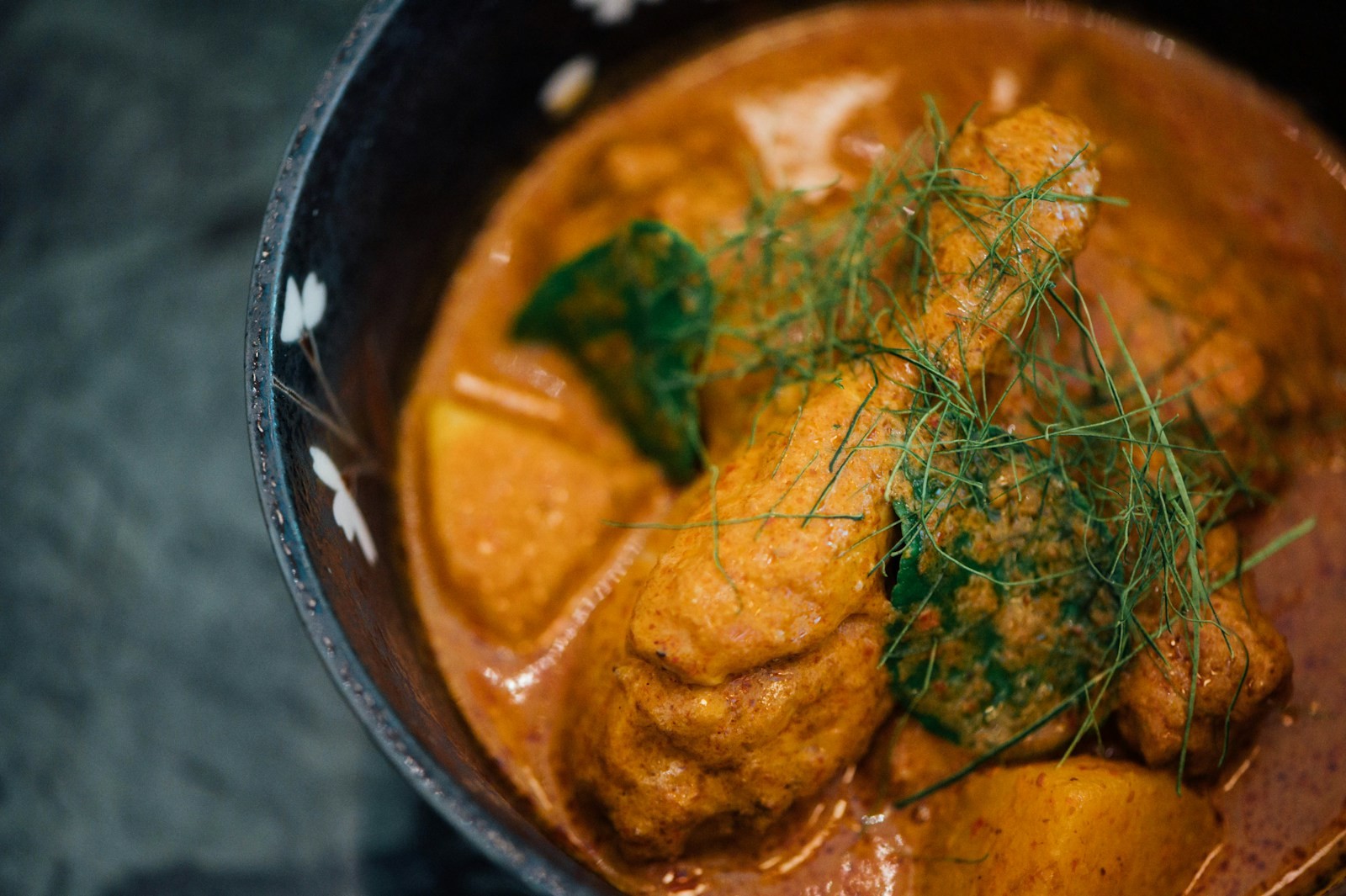 Curry with a drumstick and potato in a dark bowl