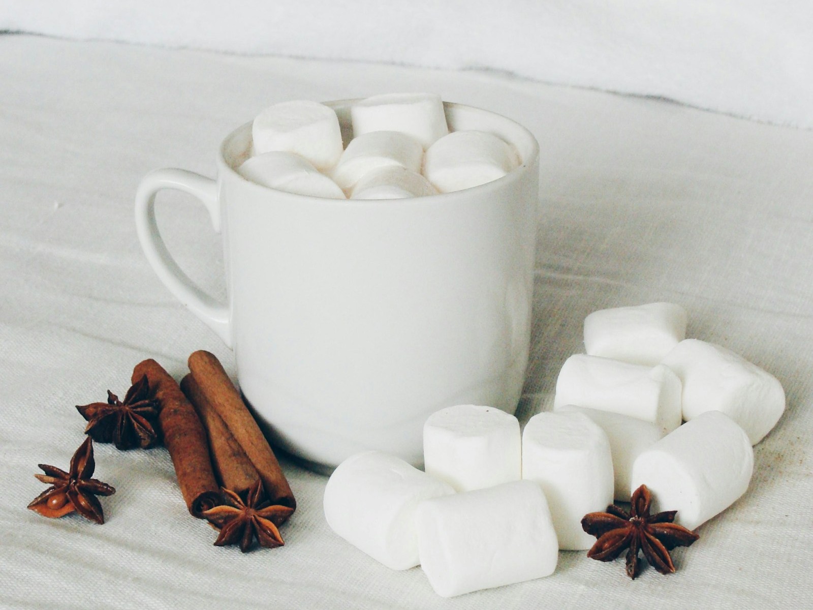White mug of homemade marshmallows with cinnamon sticks and star anise